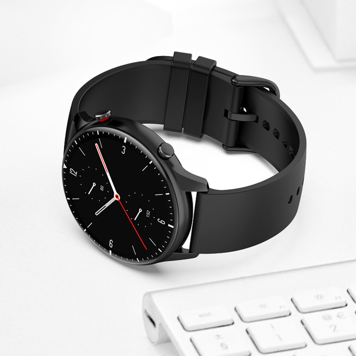 Eine schwarze Smartwatch mit schwarzem Armband liegt auf einer weißen Oberfläche. Das Zifferblatt zeigt Zahlen und Zeiger.