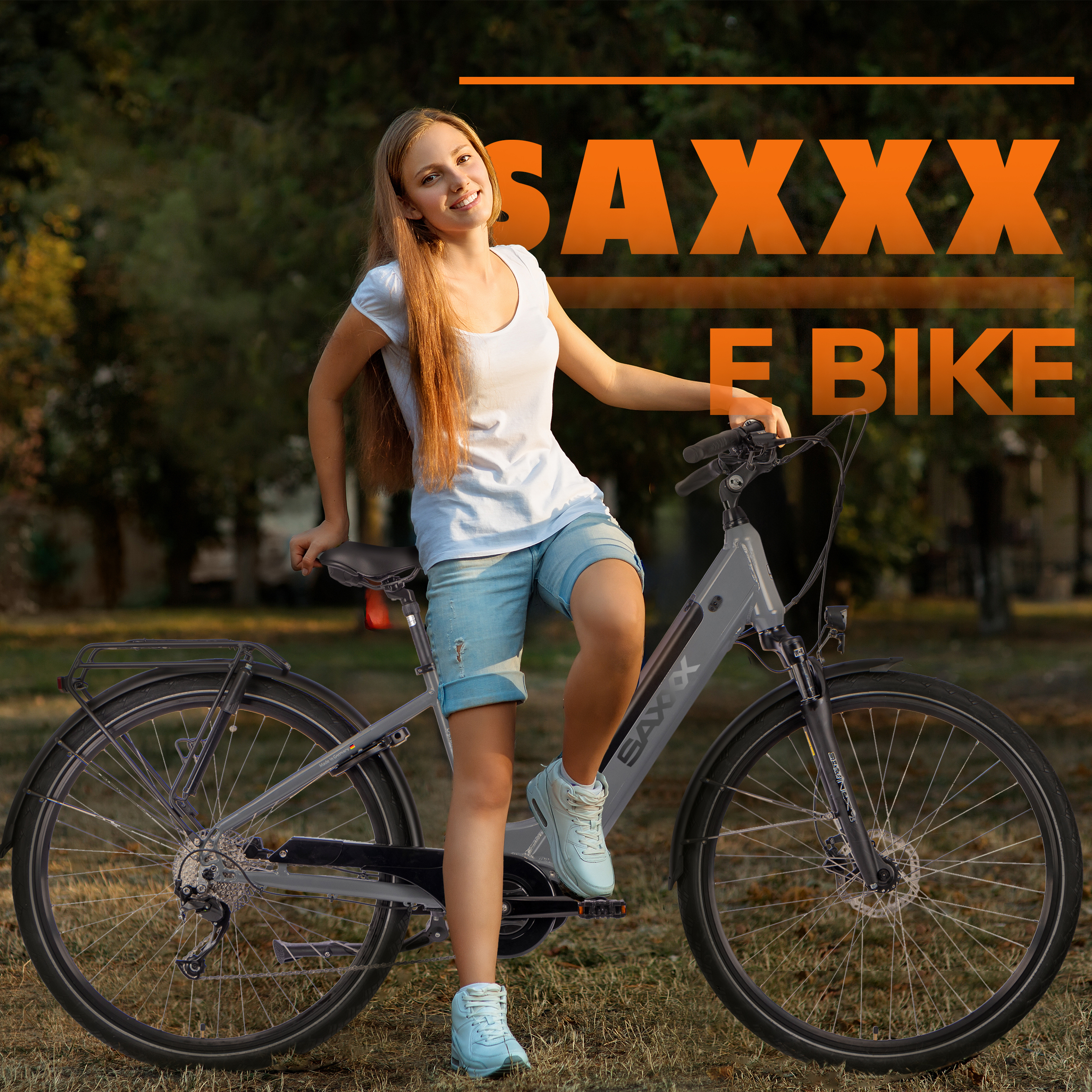 Eine junge Frau lächelt und lehnt sich in einem Park an ein graues E-Bike. Das Fahrrad hat SAXXX E BIKE Text.