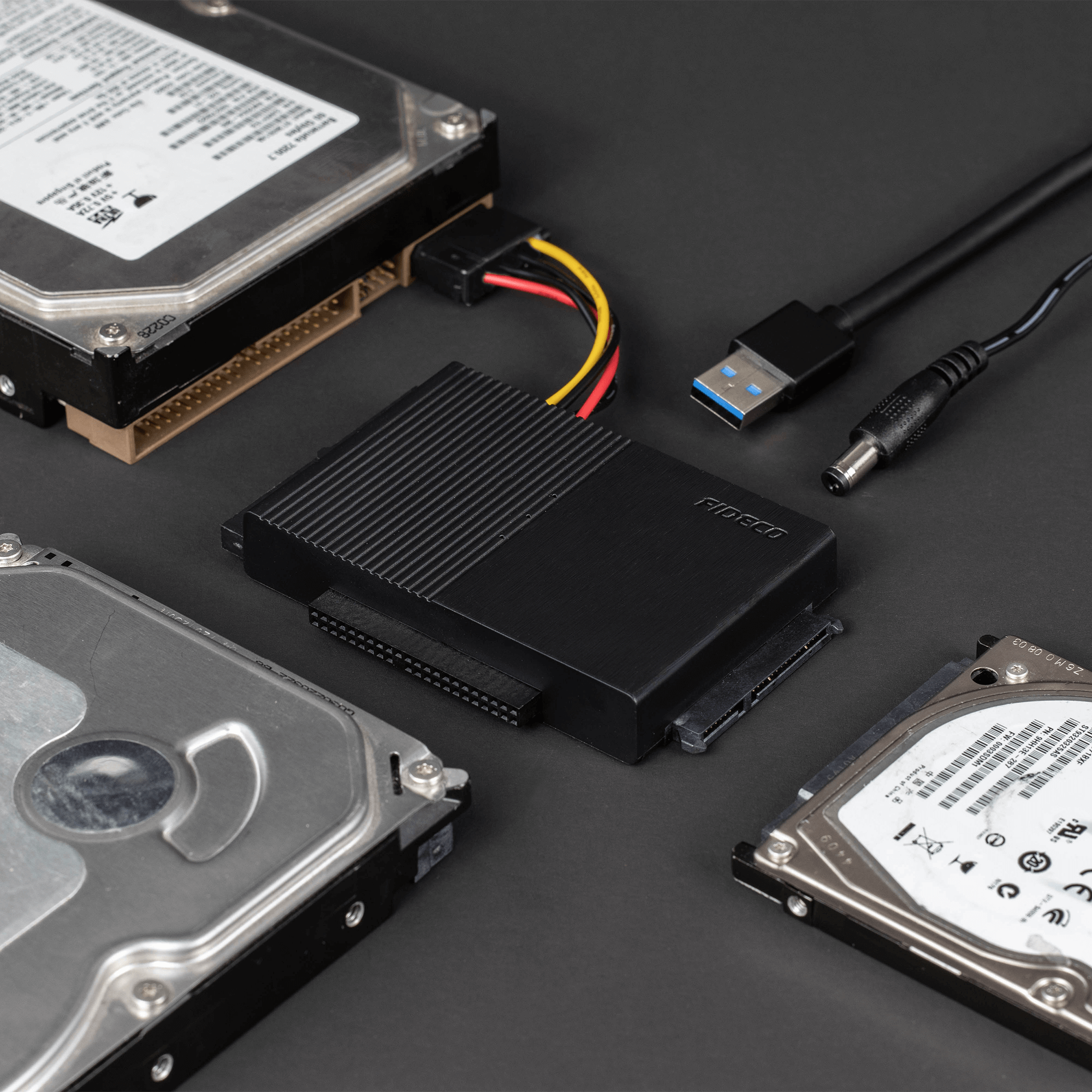 Czarny adapter dysku twardego z wieloma dyskami twardymi i kablami na ciemnej powierzchni.
