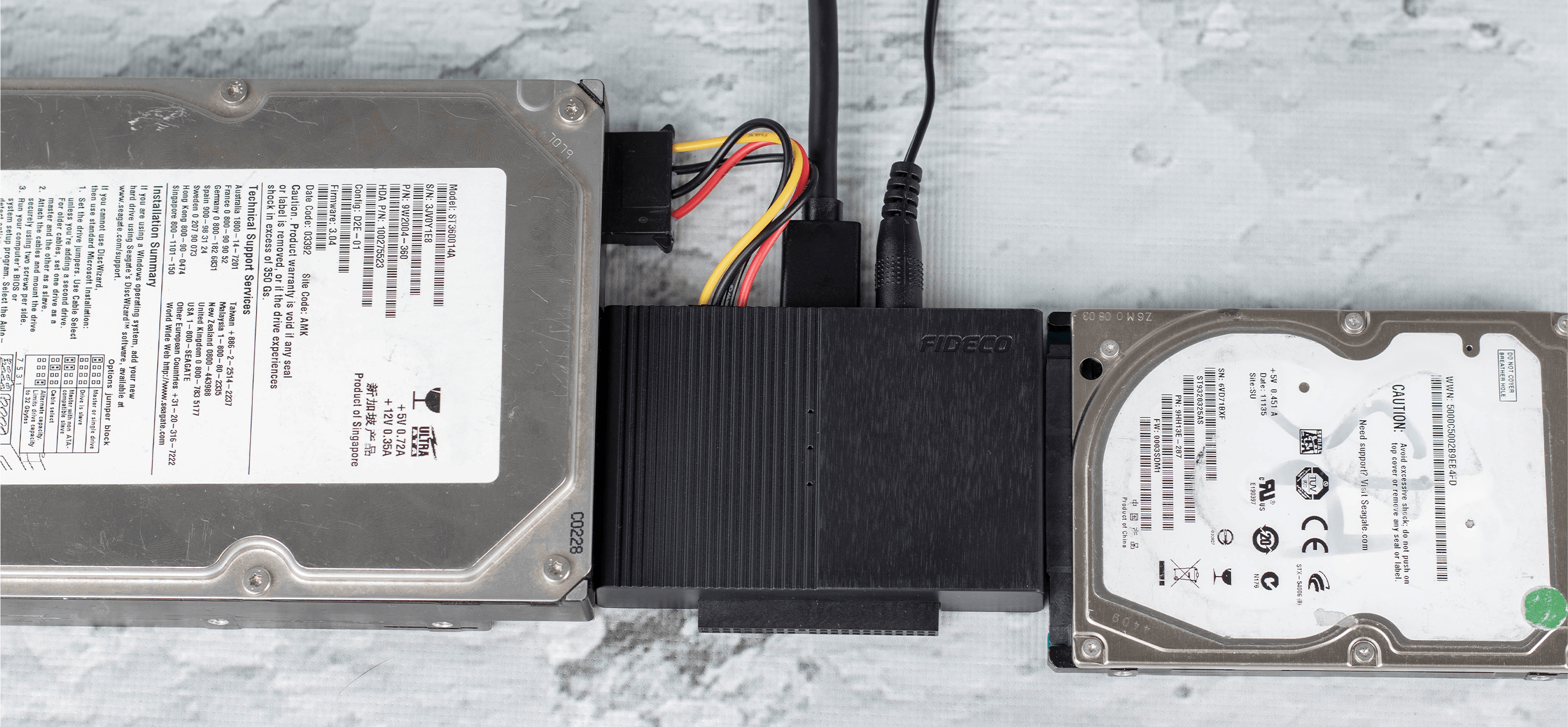 Dwa dyski twarde podłączone do czarnego adaptera. Konfiguracja znajduje się na białej powierzchni.