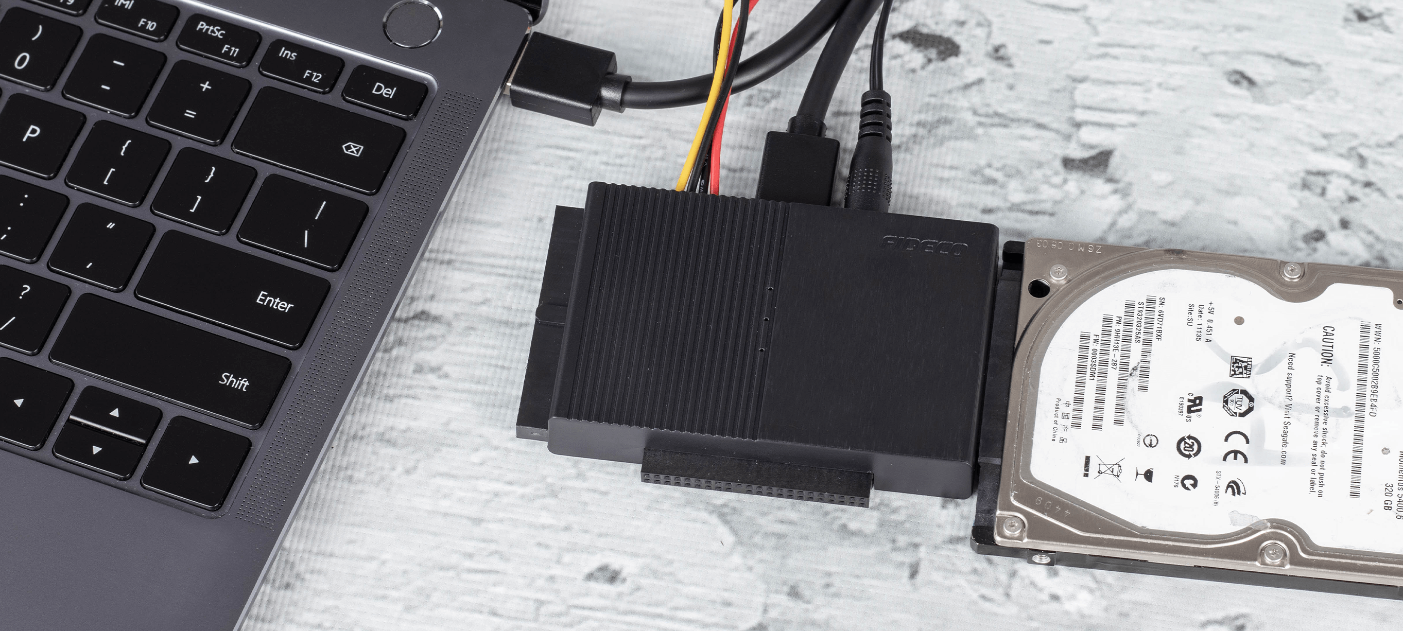 Klawiatura laptopa, czarna zewnętrzna obudowa dysku twardego i dysk twardy połączone kablami na drewnianej powierzchni.