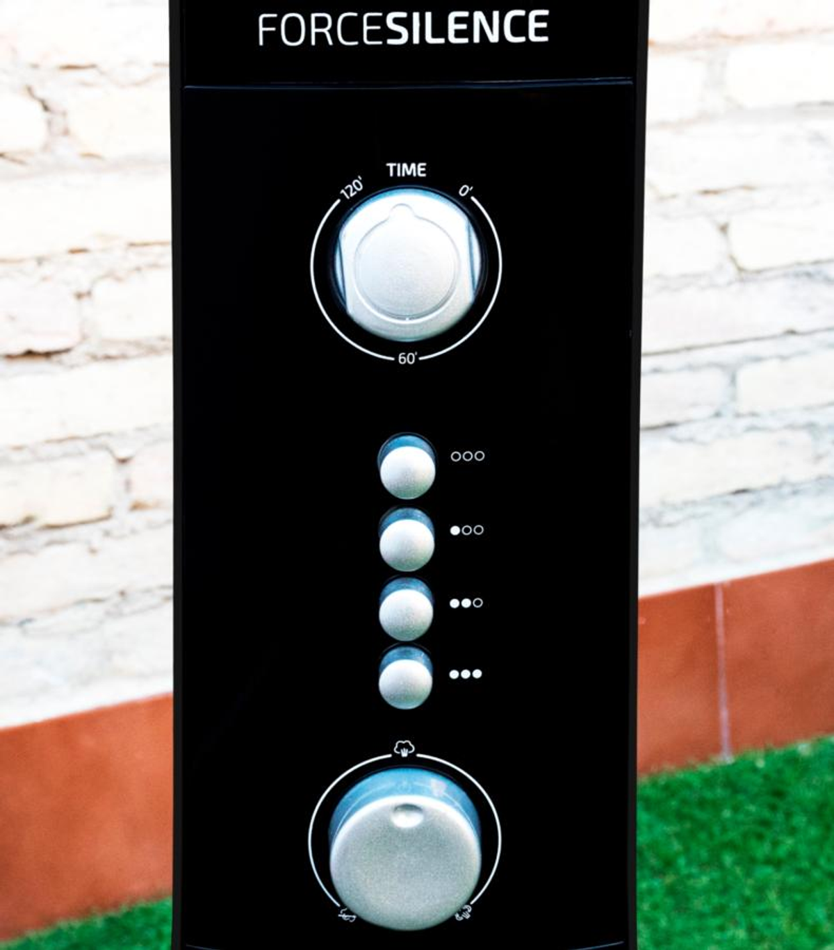 Primer plano de controles de ventilador negro con ajustes de tiempo y botones de encendido, fondo de pared de ladrillo blanco.