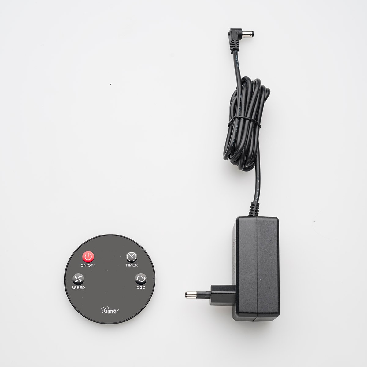 A black remote control panel with buttons and a power adapter. There is a circular control panel.