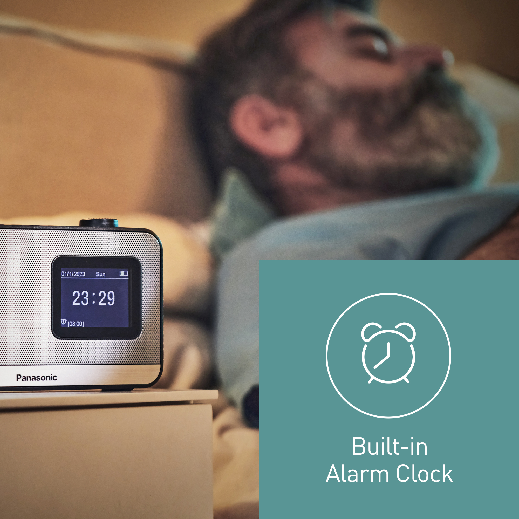 Un uomo a letto con una radiosveglia Panasonic su un comodino. L'orologio mostra l'ora e la data.