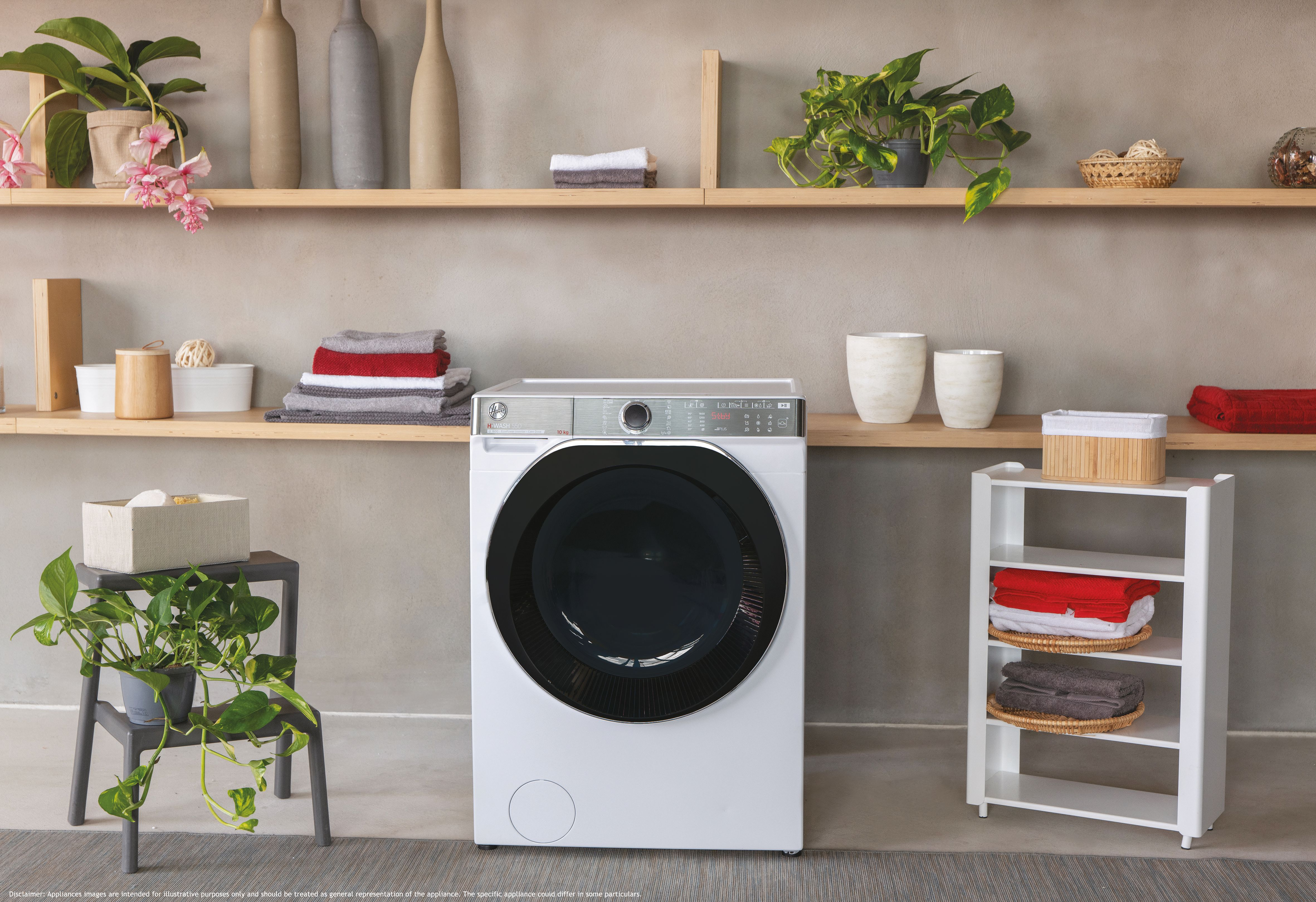Lavadora centrada entre estantes con plantas, toallas y artículos decorativos en una habitación.