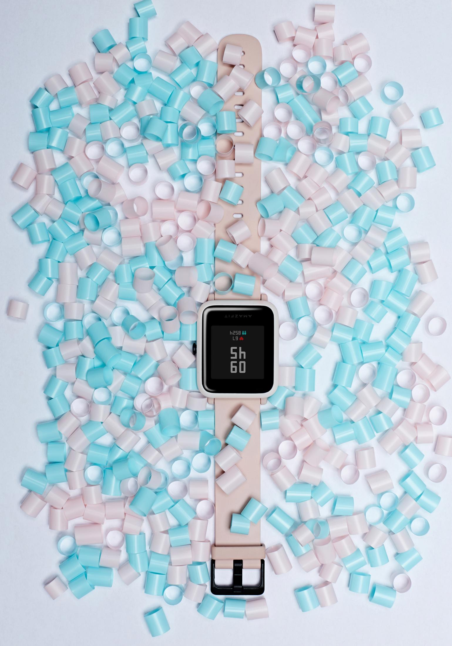 Un reloj con una banda color melocotón está rodeado de cuentas rosas y azules sobre un fondo blanco.