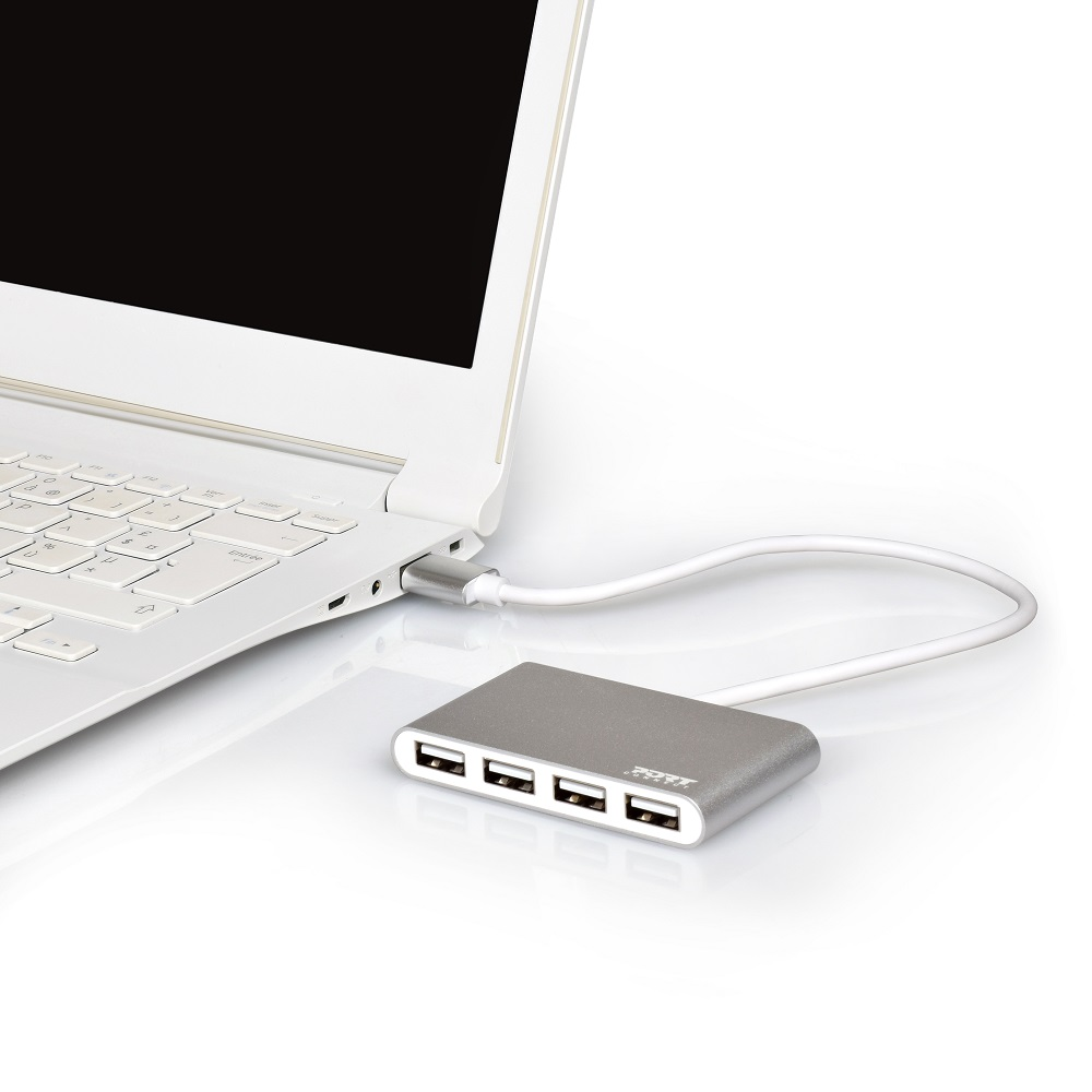 Un laptop bianco collegato a un hub USB argentato con quattro porte, su una superficie bianca.