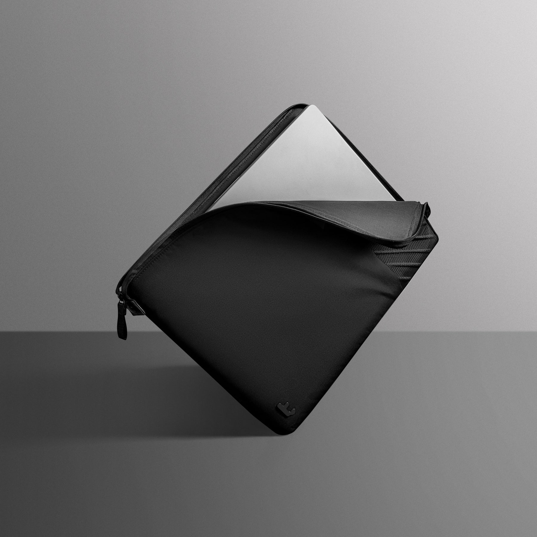 Czarna osłona na laptopa, częściowo otwarta, pokazująca laptopa w środku. Szare tło, perspektywa ukośna.