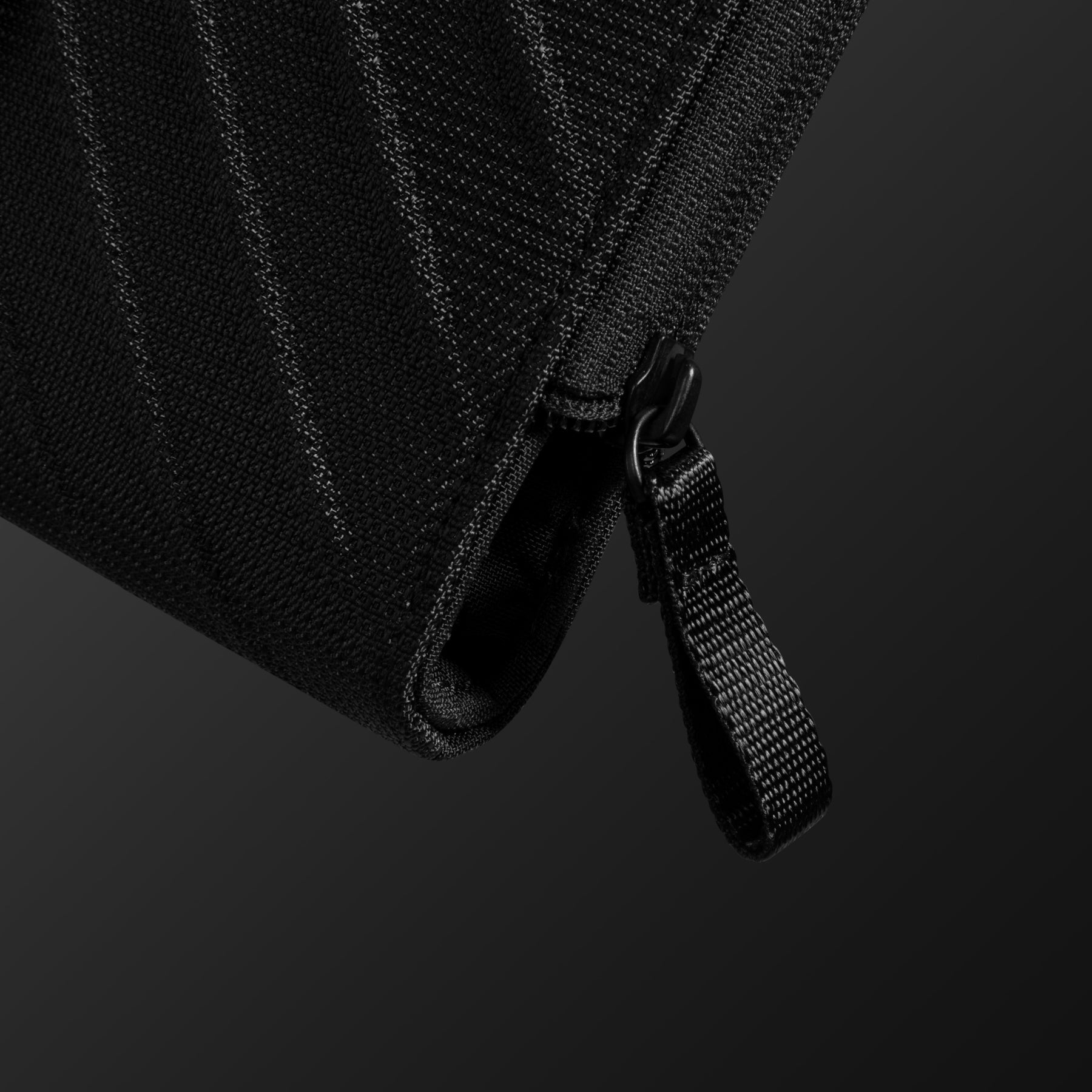 Zbliżenie czarnego suwaka na czarnej, teksturowanej tkaninie, z ciemnym tłem.