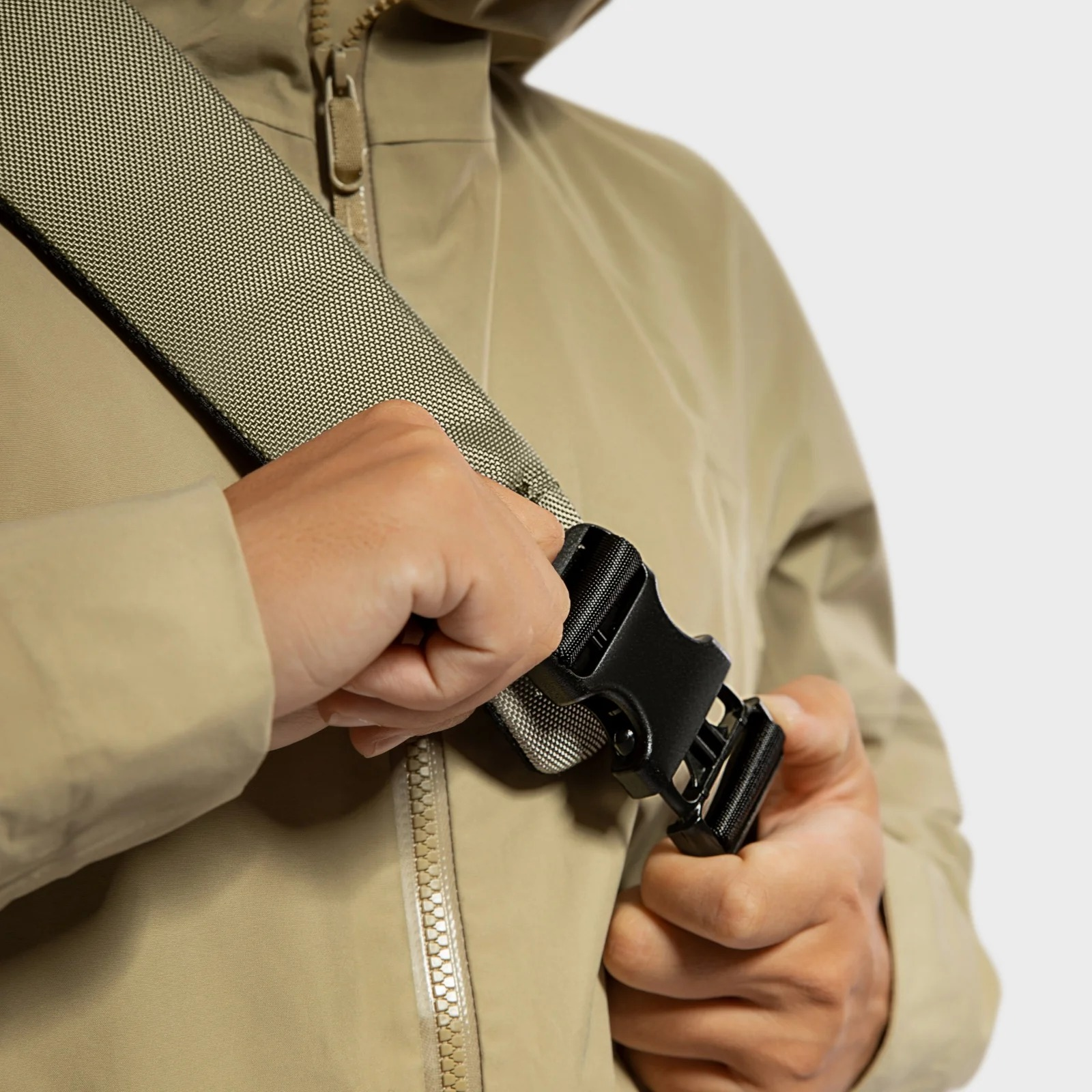 Osoba zapina czarną klamrę na beżowym pasku torby. Tło: beżowa kurtka.