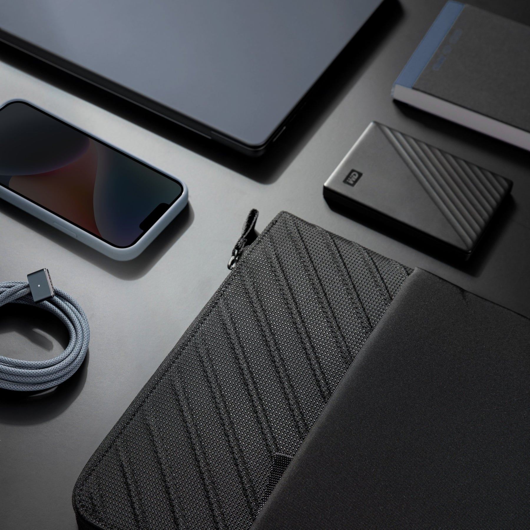 Telefon, tablet, zewnętrzny dysk twardy, kabel i czarna torba na laptopa na czarnej powierzchni.