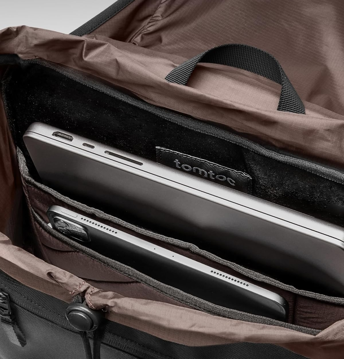 Otwarty środek torby z laptopem i tabletem w środku. Torba jest brązowa. Widoczna jest nazwa marki 'tomtoc'.