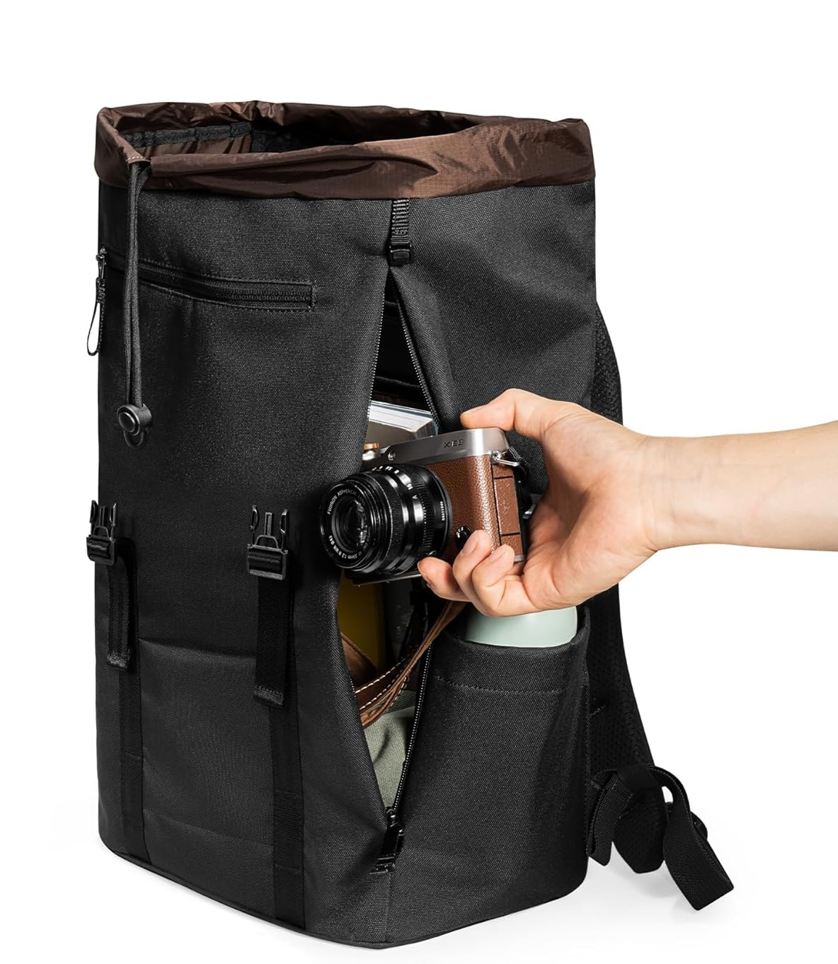 Osoba wkładająca aparat do czarnego plecaka. Torba jest czarna z brązową górą.