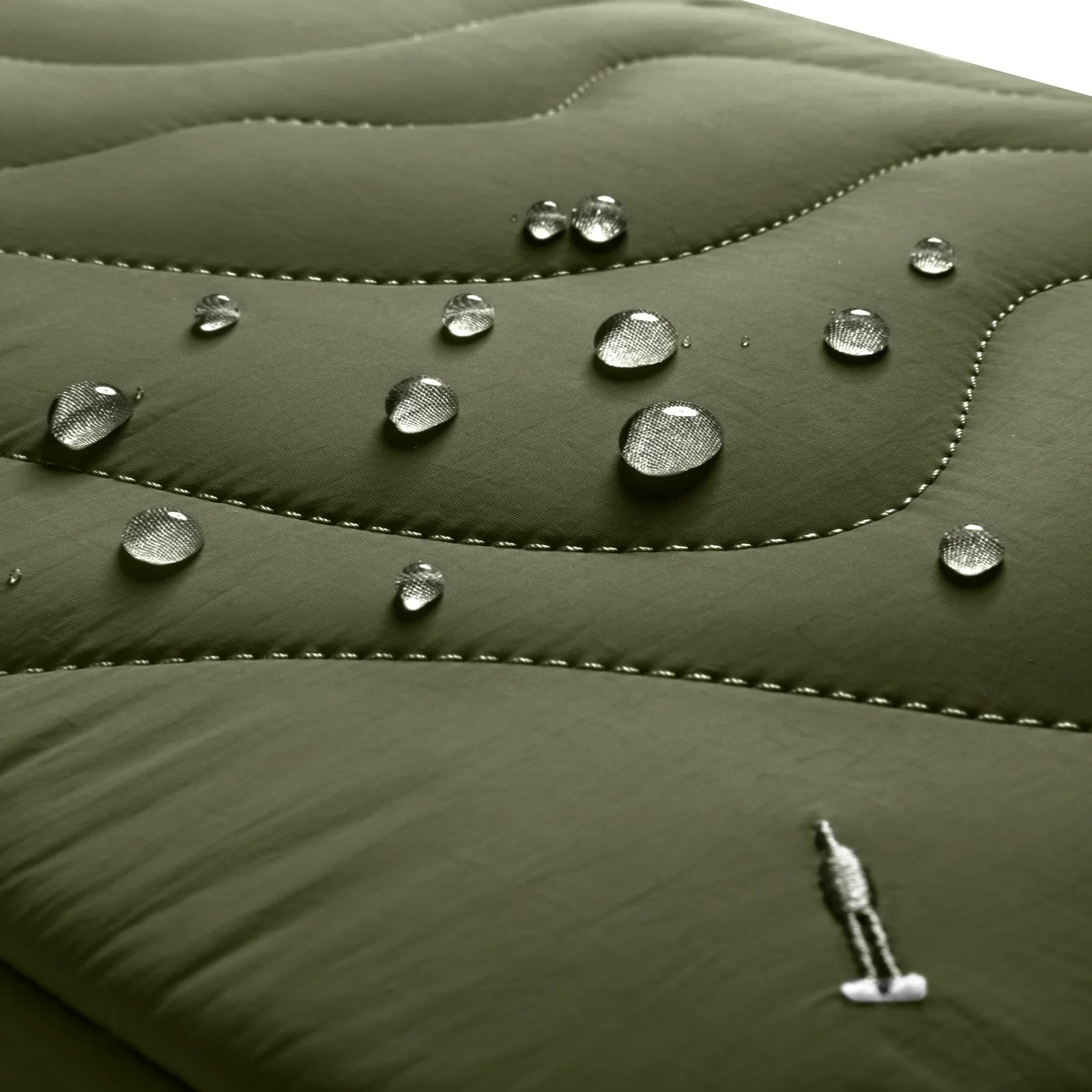 Zbliżenie na zieloną pikowaną tkaninę z kroplami wody. Małe logo osoby jest wszyte w tkaninę.