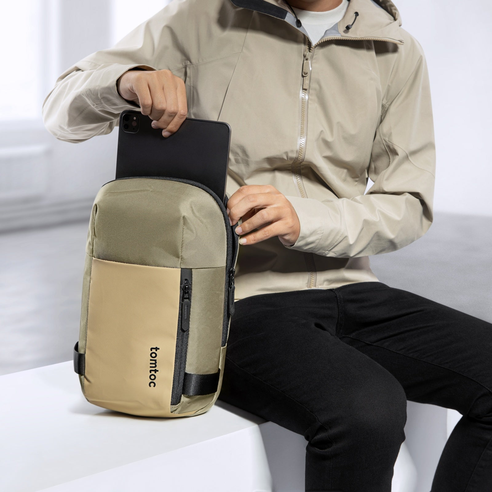 Osoba wkładająca tablet do beżowo-czarnej torby na ramię. Torba ma nazwę marki 'tomtoc'.