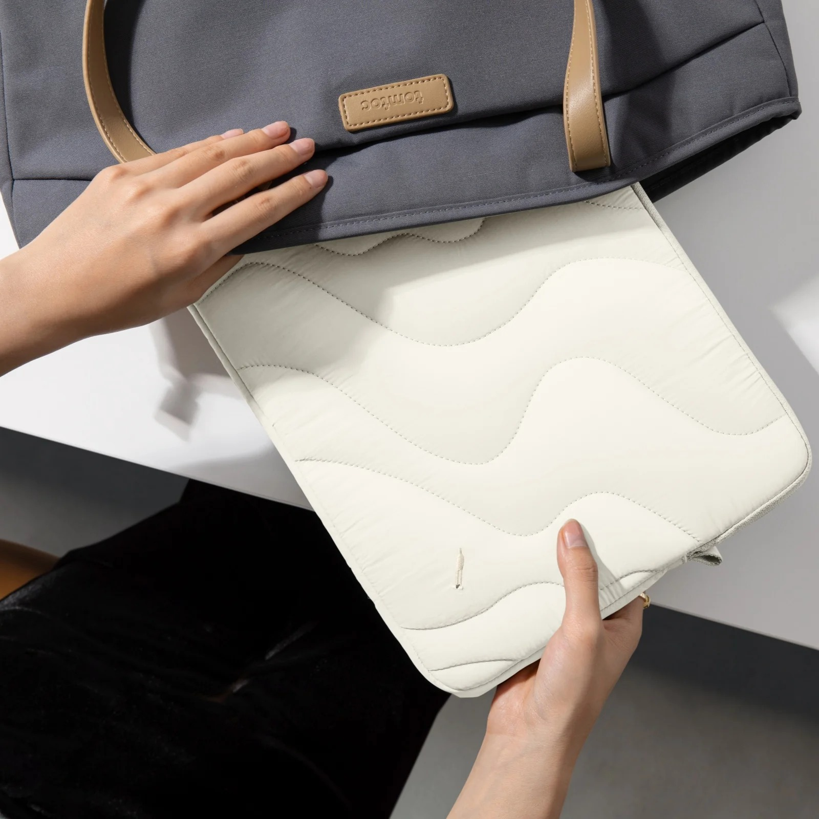 Ręce umieszczają białą pikowaną osłonę na laptopa w szarej torbie na białej powierzchni.