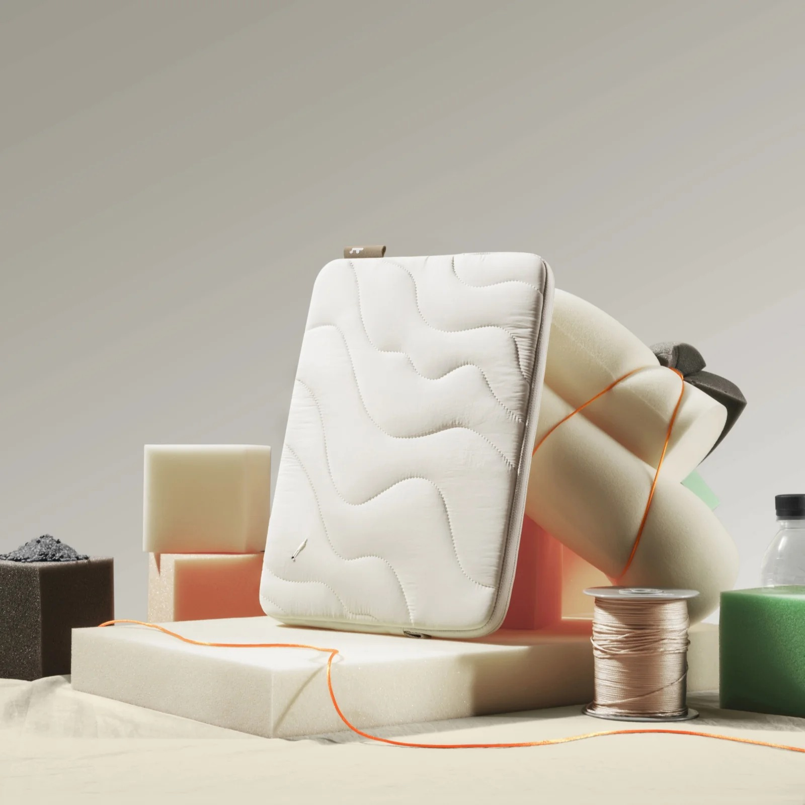 Biała pikowana osłona na laptopa z pianką i materiałami do szycia. Fotografia produktu.