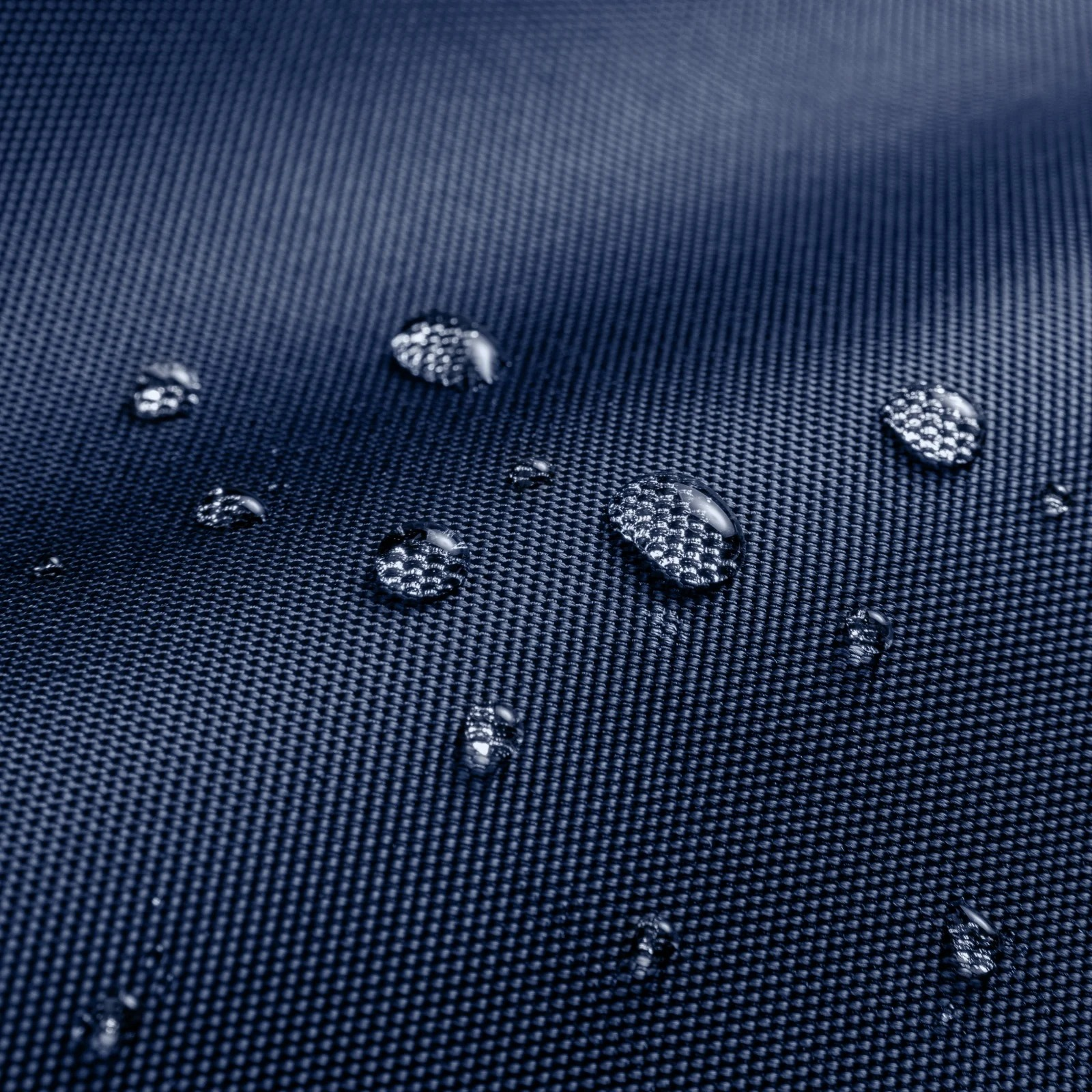 Zbliżenie granatowej tkaniny z kroplami wody. Krople są przezroczyste, odbijają światło i różnią się rozmiarem.