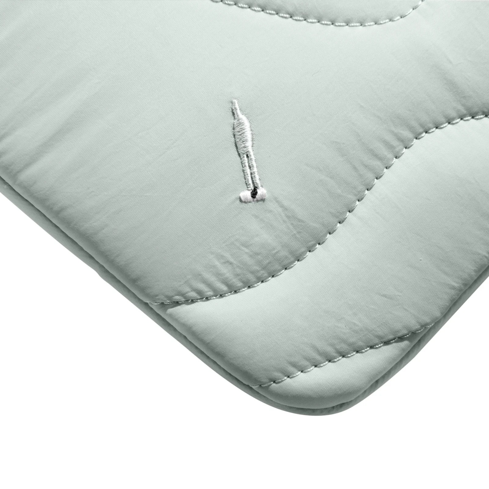 Zbliżenie na jasnozielony, pikowany materiał z małym, haftowanym detalem.