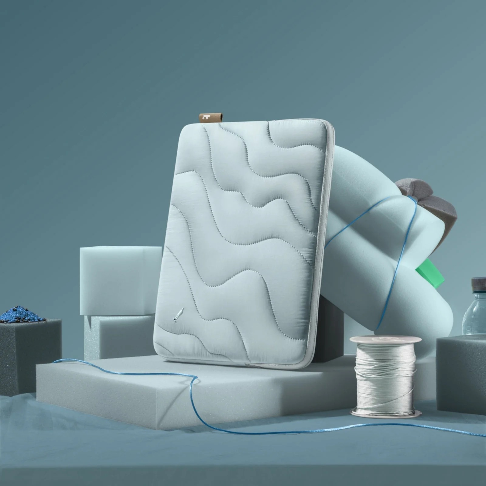 Jasnoszara pikowana torba na laptopa stoi na kostce. Widoczne są inne kształty piankowe i szpulka nici.