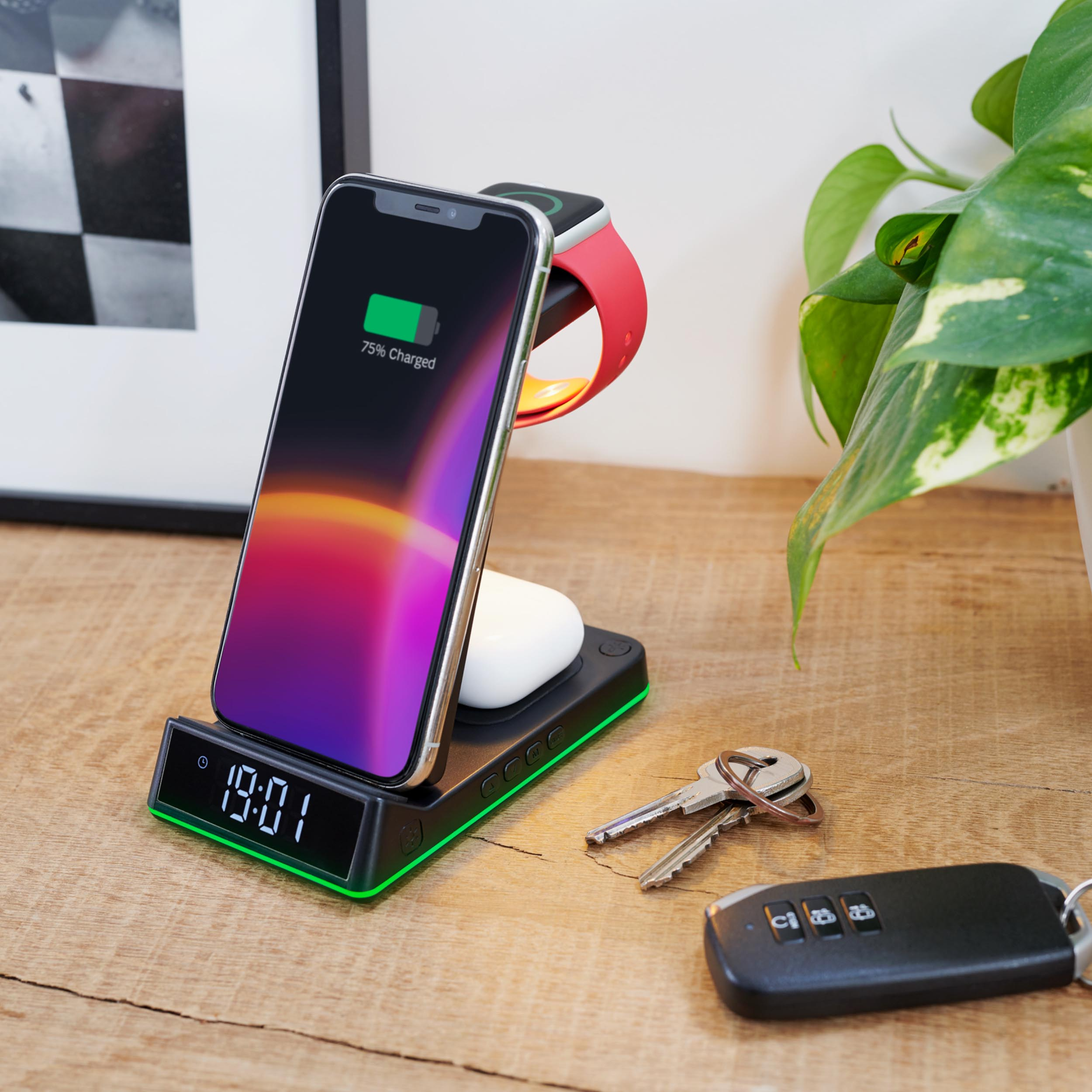 Stacja ładująca trzyma telefon, zegarek i słuchawki. Obok znajduje się zestaw kluczy i roślina.