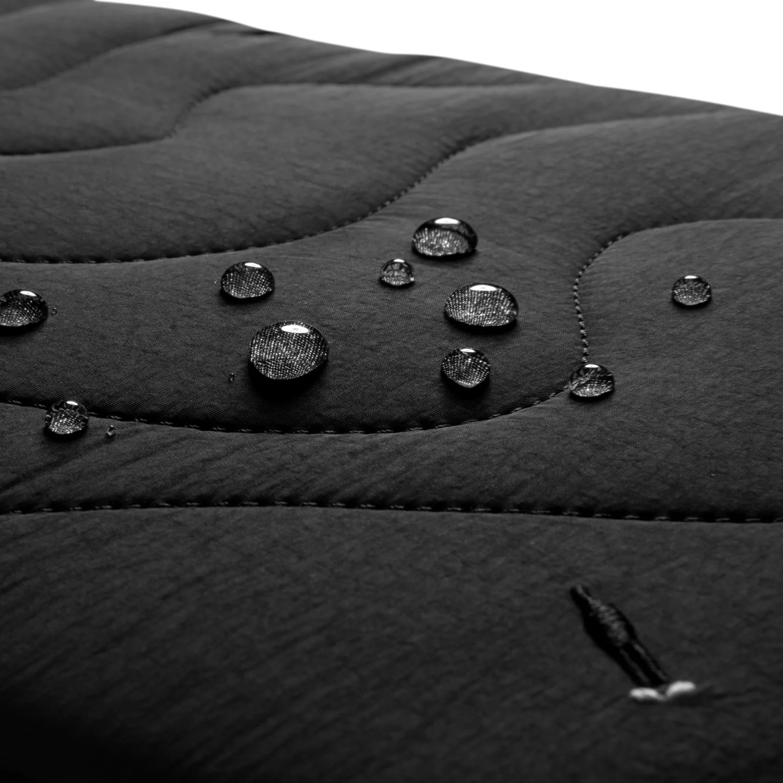 Zbliżenie czarnej pikowanej tkaniny z kroplami wody. Widoczny mały detal ściegu.