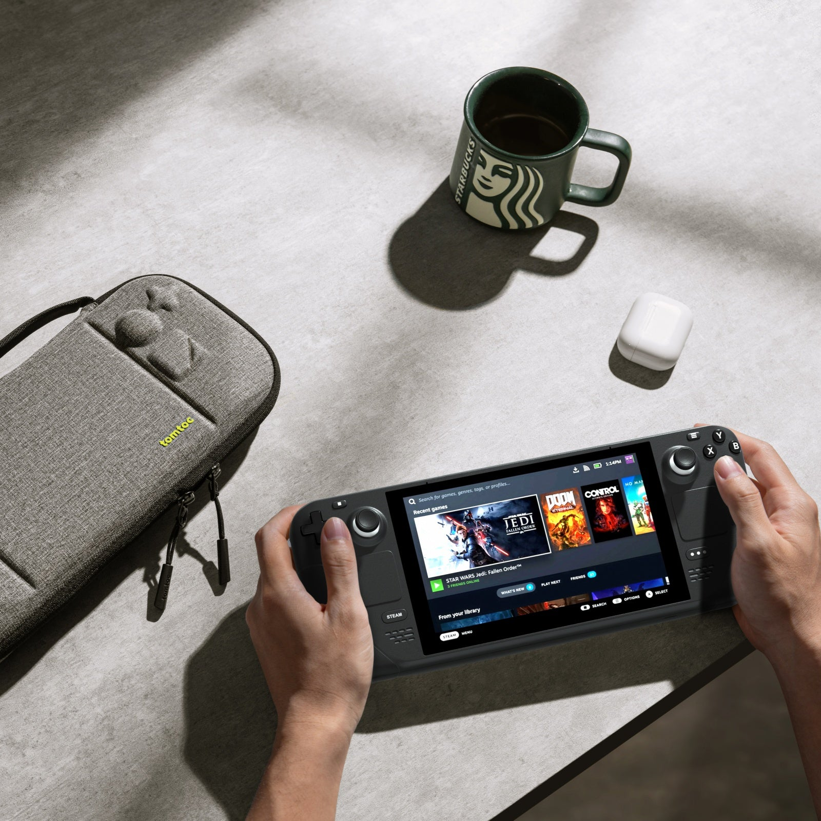 Osoba trzyma konsolę do gier. Konsola jest włączona, z etui i kubkiem w pobliżu.