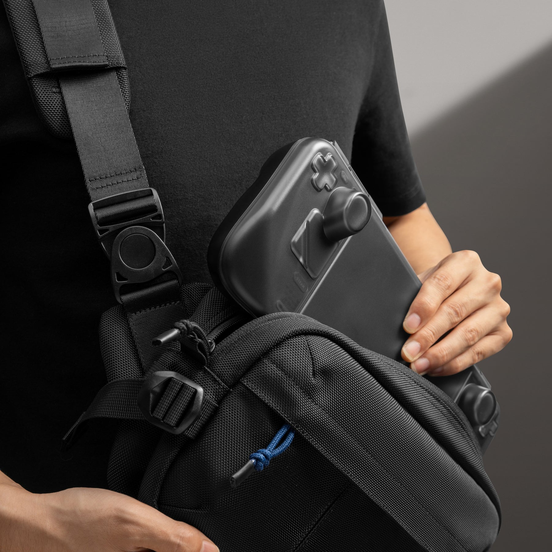 Osoba trzymająca kontroler do gier w czarnej torbie na ramię z paskami i klamrami.