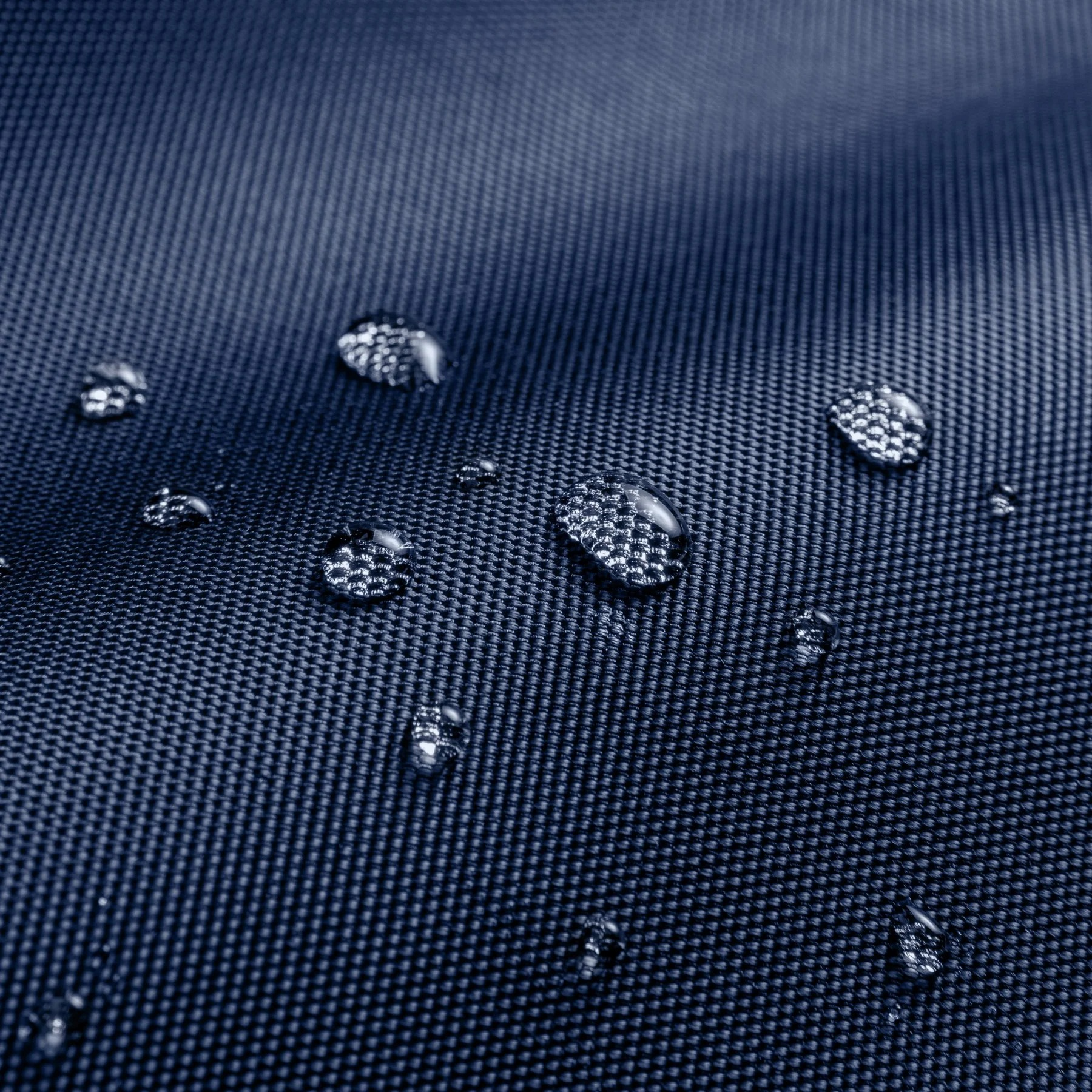 Zbliżenie kropli wody na ciemnoniebieskiej, teksturowanej tkaninie. Odbicia światła.