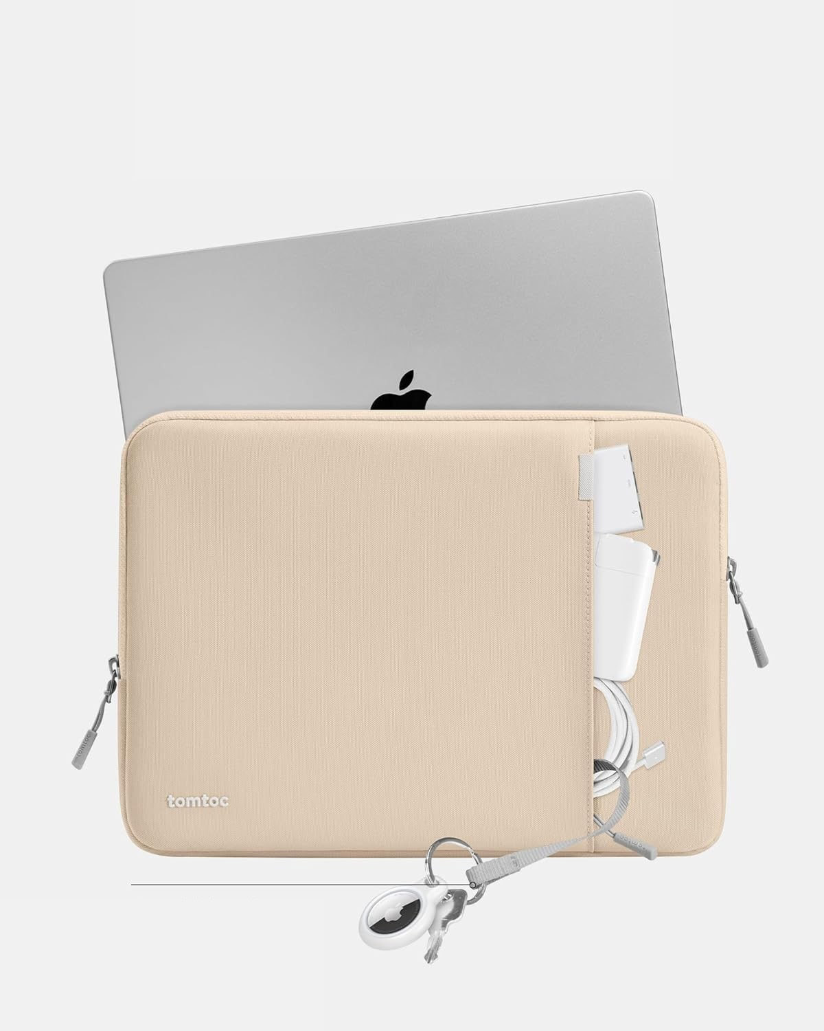 Beżowa torba na laptopa zawierająca laptopa, ładowarkę i akcesoria. Białe tło.