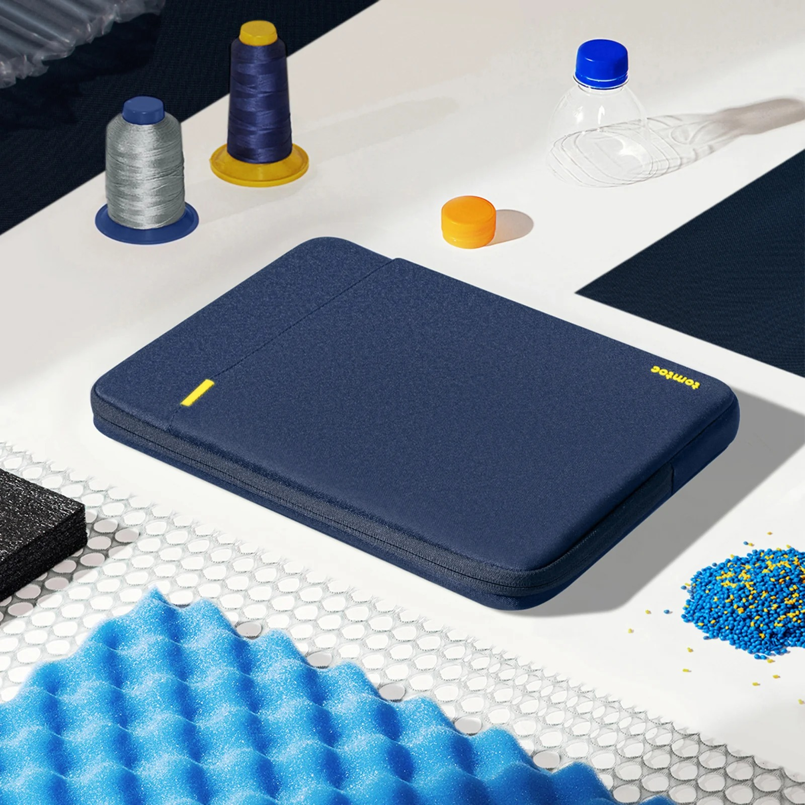 Układ granatowej torby na laptopa z akcesoriami do szycia, plastikową butelką i pianką. Widok z góry.