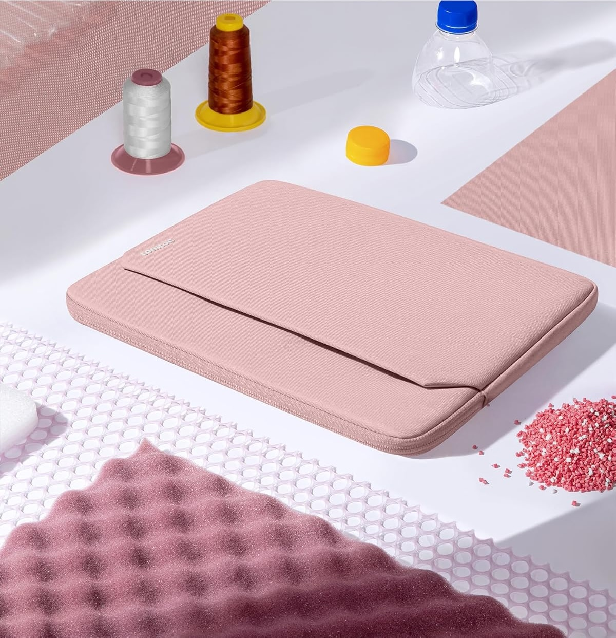 Różowa torba na laptopa z akcesoriami do szycia na białej powierzchni. Scena jest dobrze oświetlona.