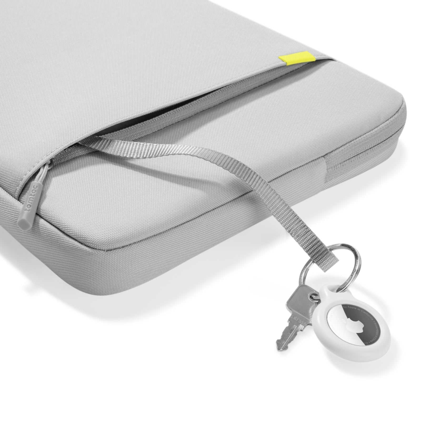 Szary pokrowiec na laptopa. Dołączone klucze i AirTag. Widoczna marka 'tomtoc'.