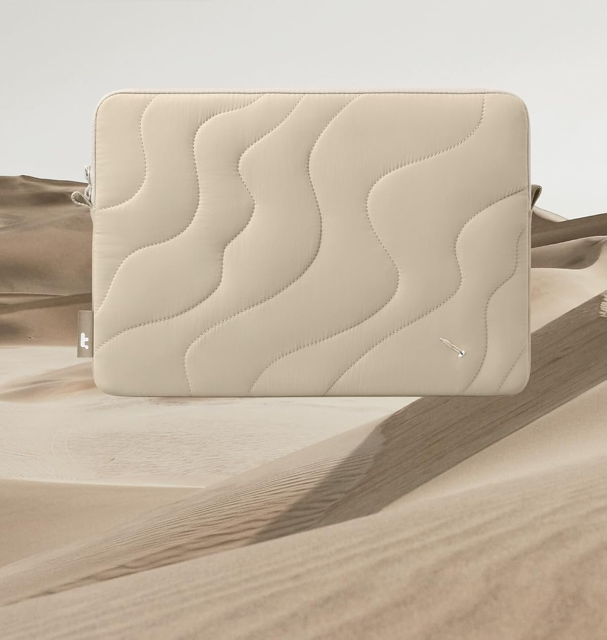 Beżowe etui na laptopa na piaszczystym tle. Widoczna marka 'tomtoc'.