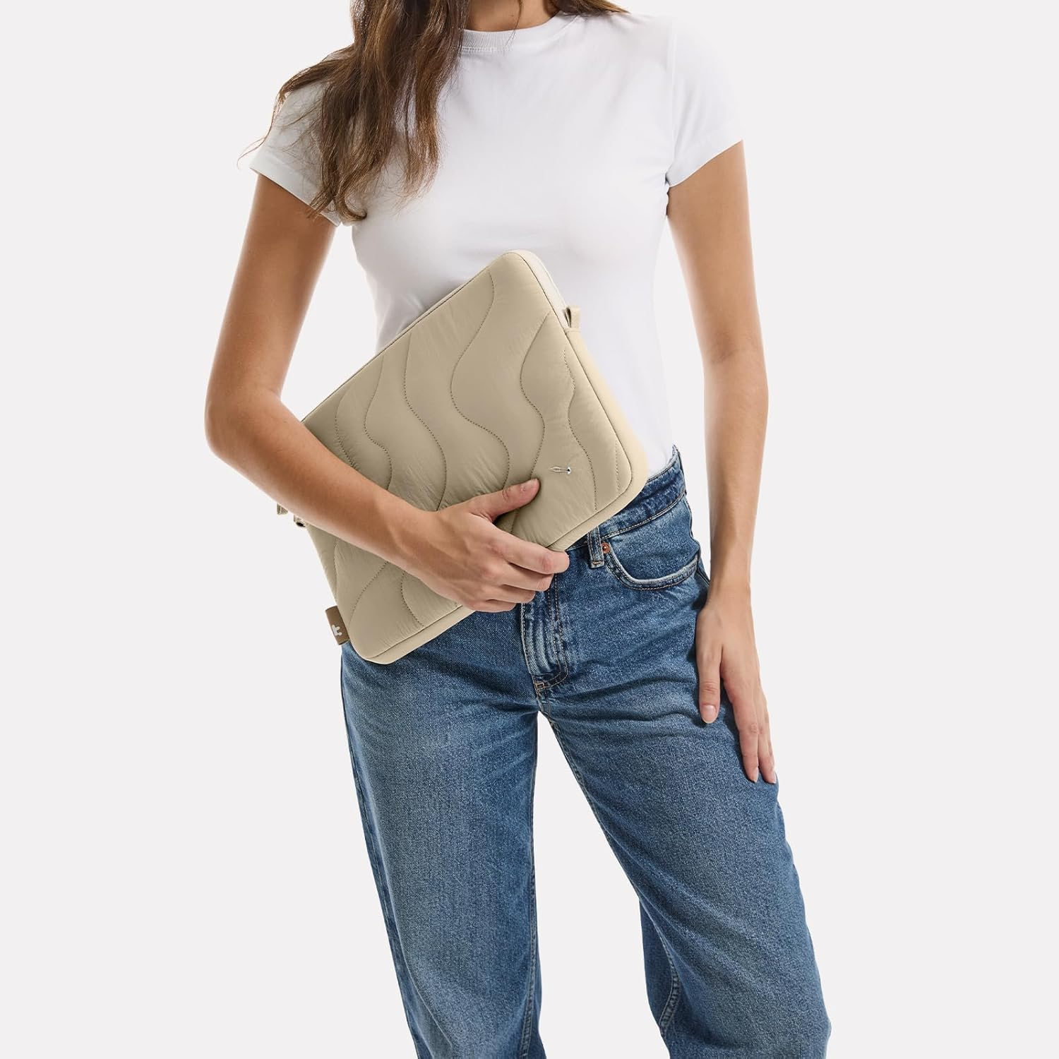 Kobieta trzymająca beżowe pikowane etui na laptopa. Ma na sobie biały t-shirt i niebieskie dżinsy.