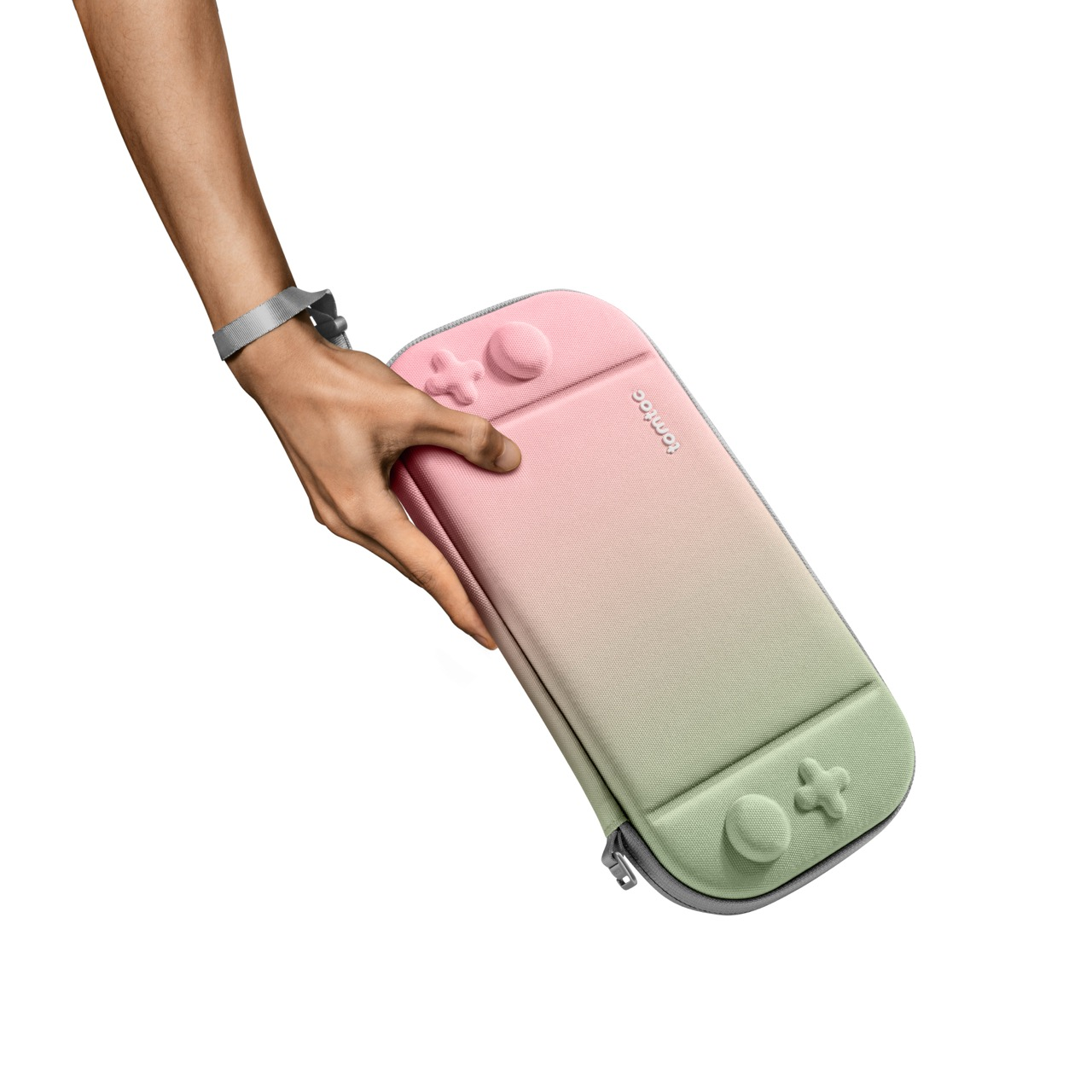 Ręka trzymająca etui Switch, gradient od zielonego do różowego. Marka widoczna.