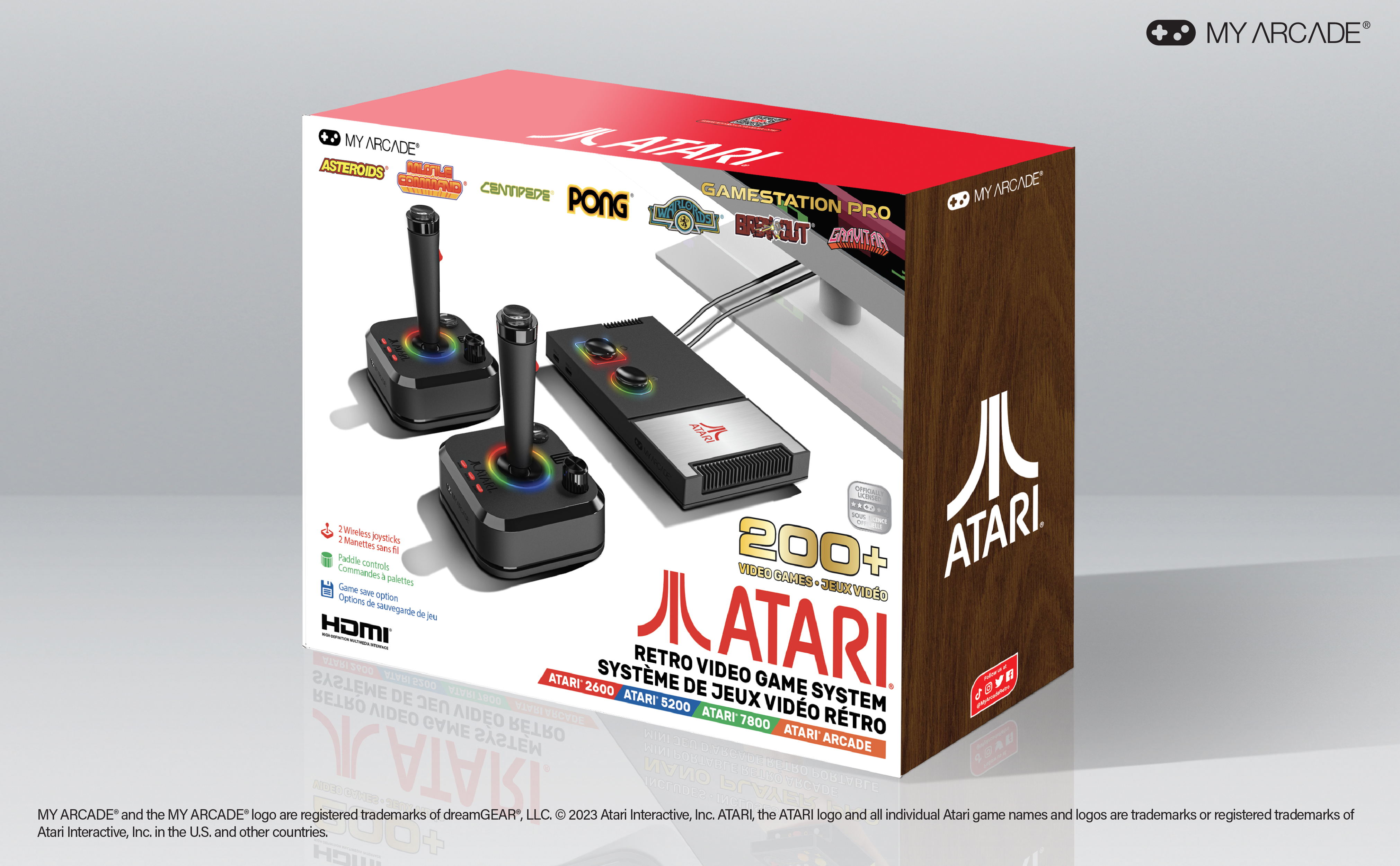 Sistema de videojuegos retro en caja con dos joysticks y una consola sobre madera. La caja tiene gráficos coloridos.