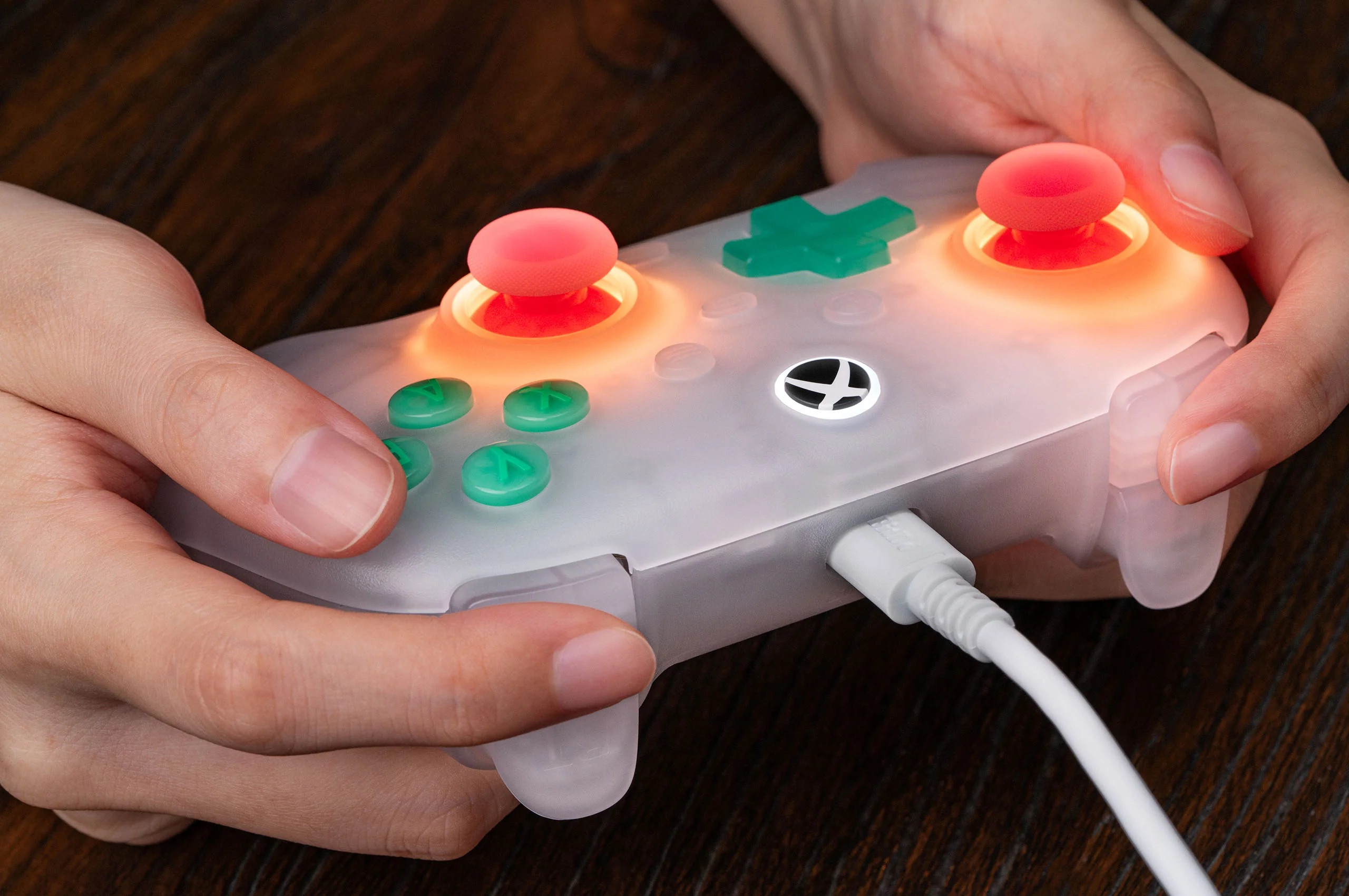 Mani che tengono un controller di gioco bianco con pulsanti luminosi e joystick rosso, collegato da cavo.