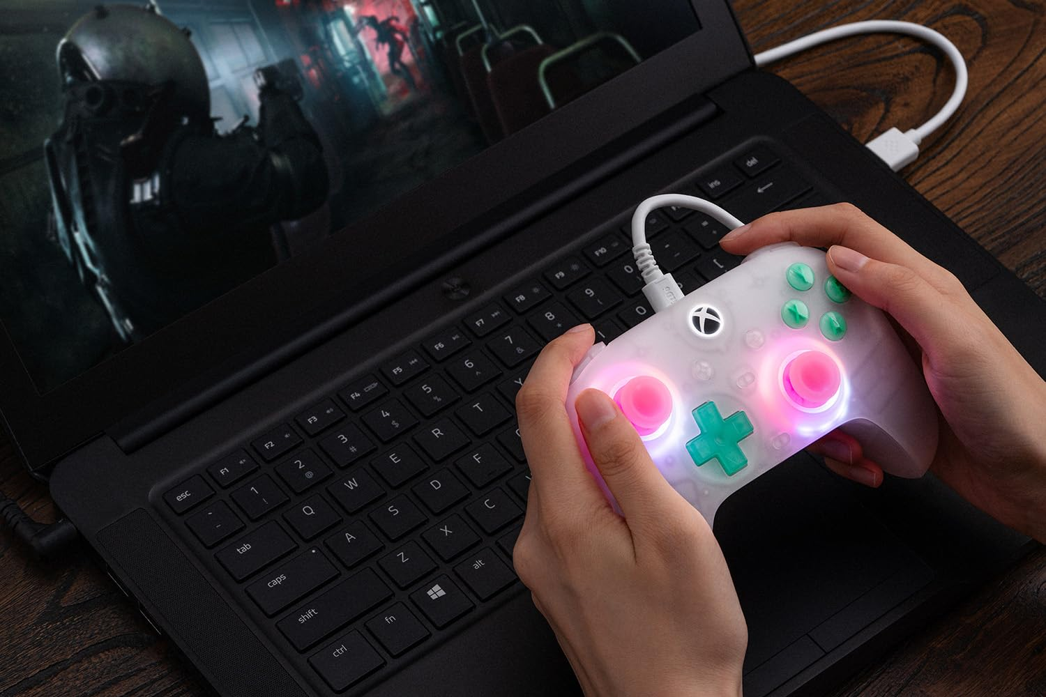 Una persona gioca a un gioco su un laptop con un controller bianco con pulsanti rosa e verdi.