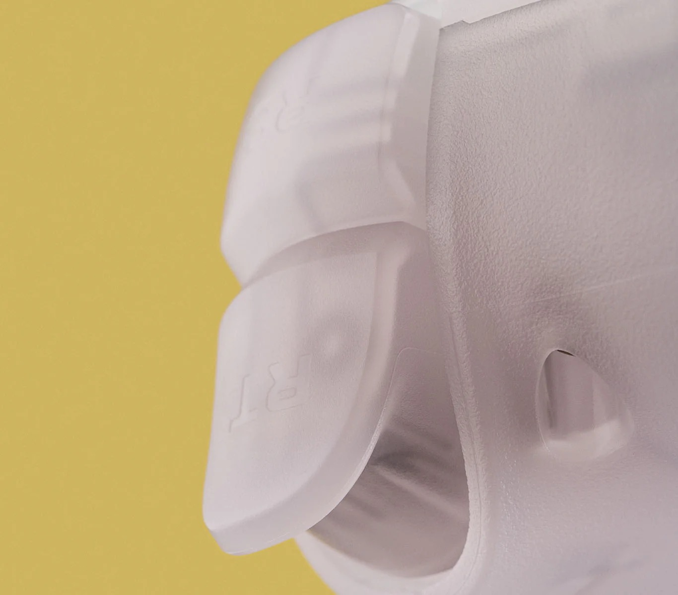 Primo piano di un componente di plastica bianca, forse parte di un dispositivo, su sfondo giallo.