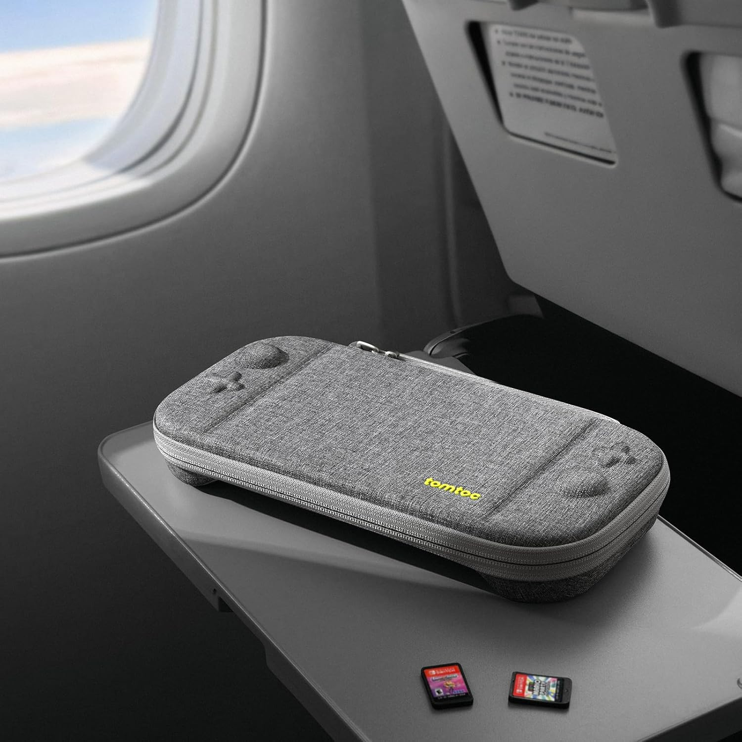 Szara obudowa Switch spoczywa na tacy. Dwa kartridże do gier poniżej. Scena ma miejsce w samolocie.
