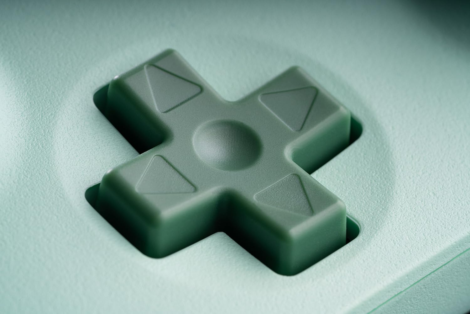 Zbliżenie zielonego przycisku w kształcie krzyża na jasnozielonej powierzchni. Przycisk przeznaczony jest do urządzenia do gier.