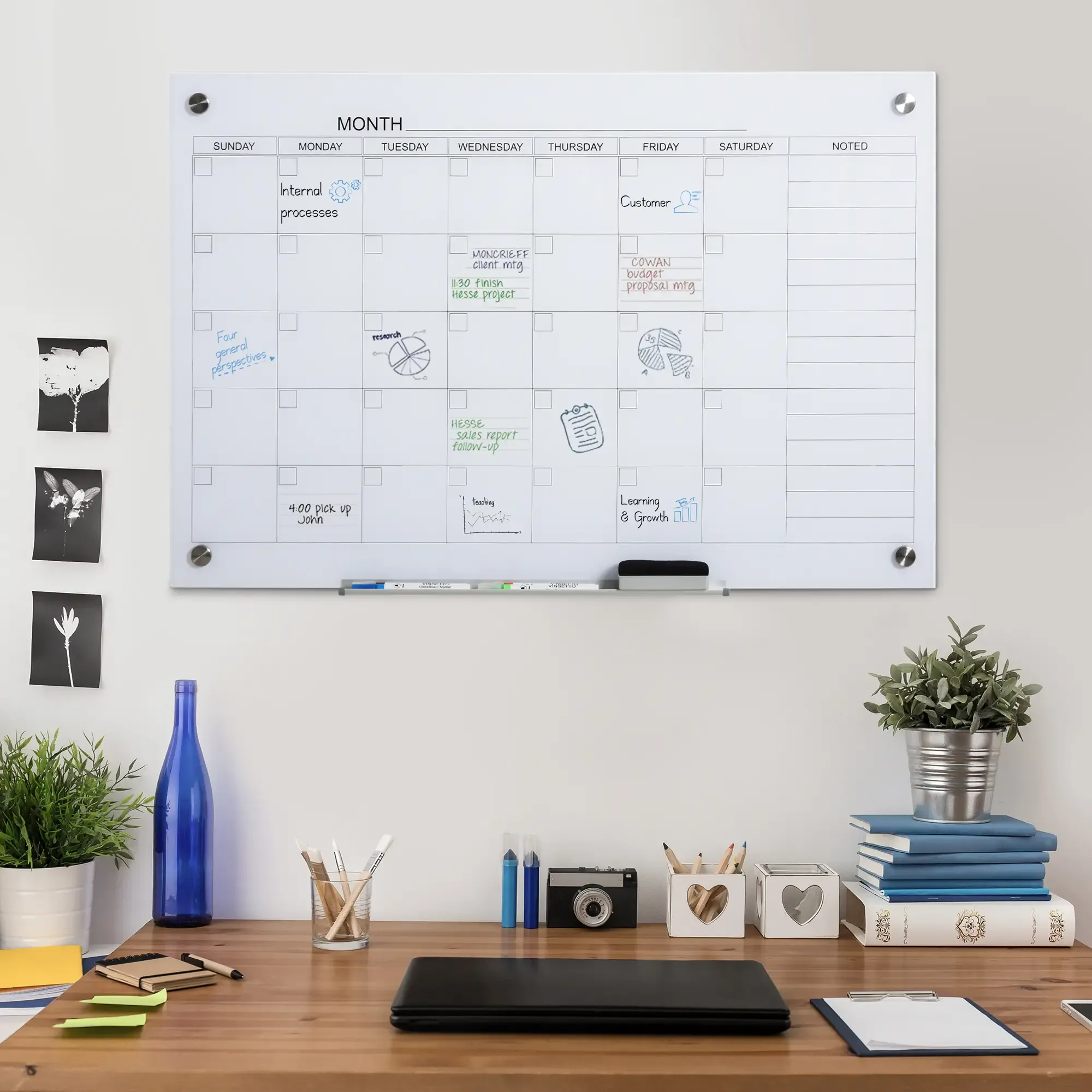 Ein Schreibtisch mit einem Whiteboard-Kalender. Notizen und Gegenstände auf dem Schreibtisch, einschließlich Pflanzen und einer blauen Flasche.