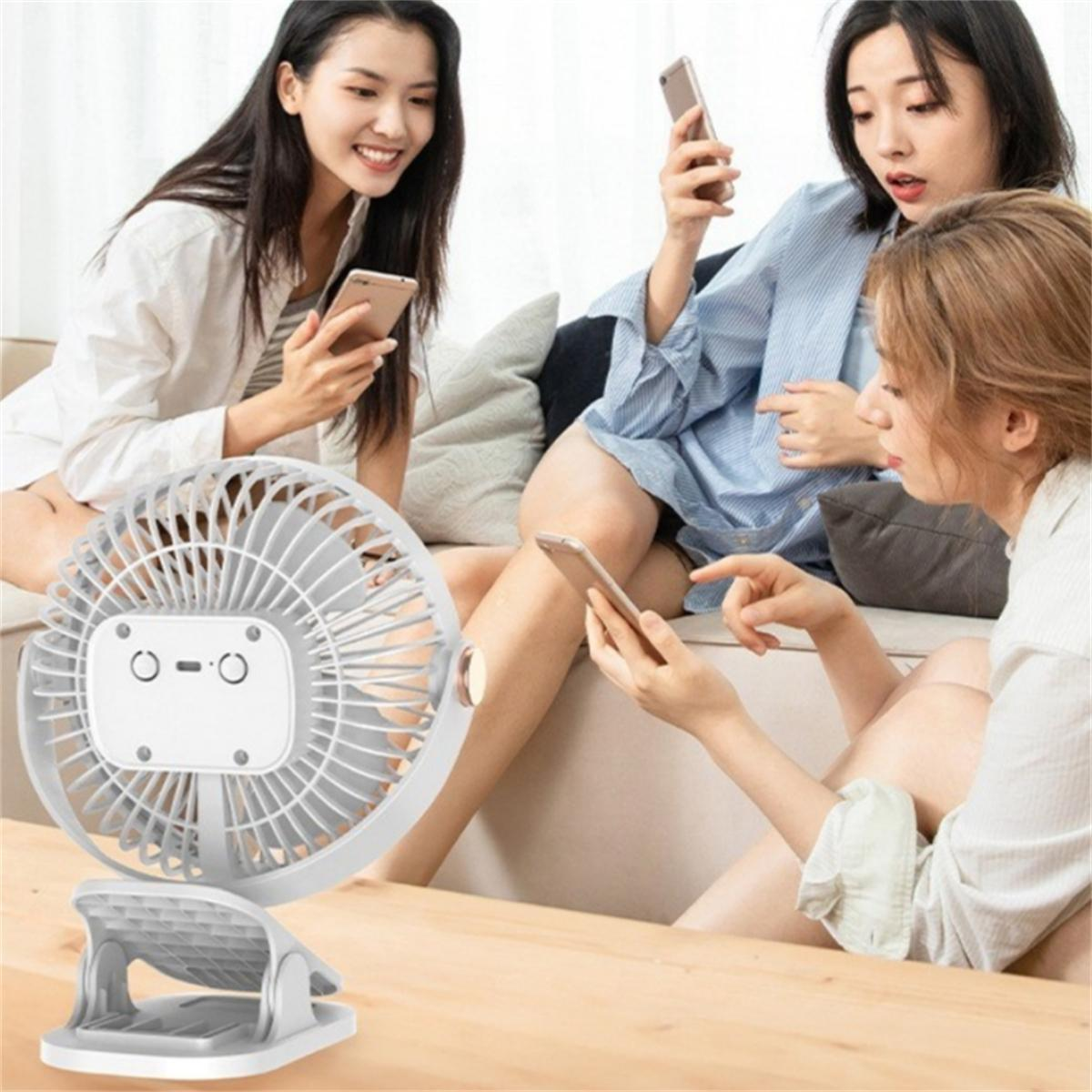 Drei Frauen sitzen auf einem Sofa und benutzen ihre Handys. Ein weißer Ventilator steht auf einem Tisch vor ihnen.