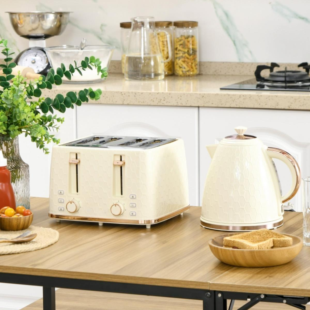 Beiger Toaster und Wasserkocher auf Holztisch. Küchenutensilien im Hintergrund. Grüne Pflanze in Glasvase vorhanden.