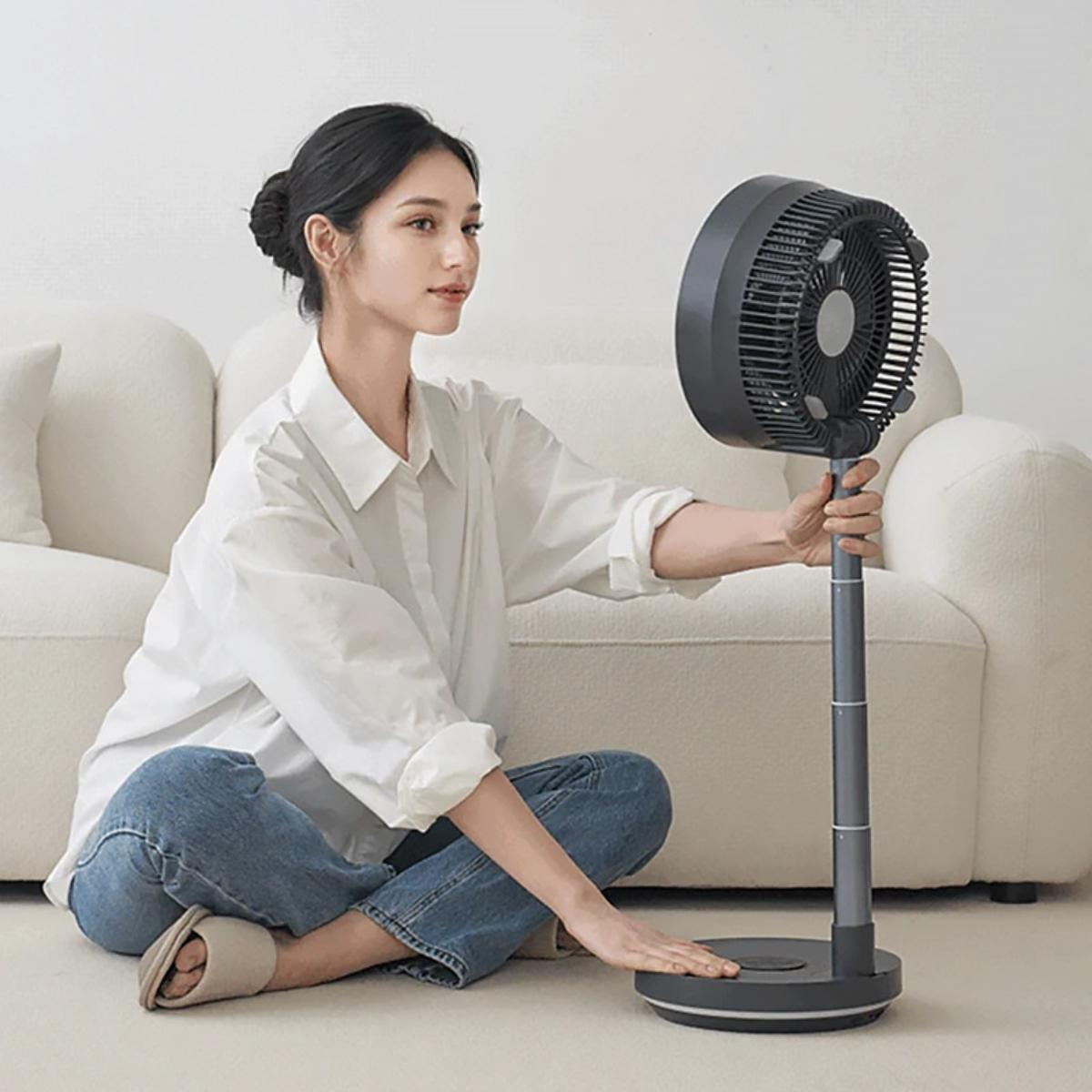 Eine Frau stellt einen grauen Ventilator auf einem Ständer ein.