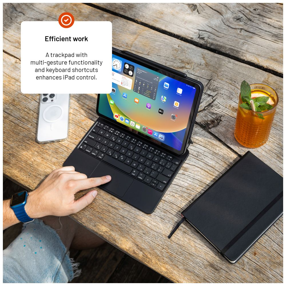 iPad mit Tastatur auf Holztisch, Telefon, Getränk und Notizbuch sichtbar.