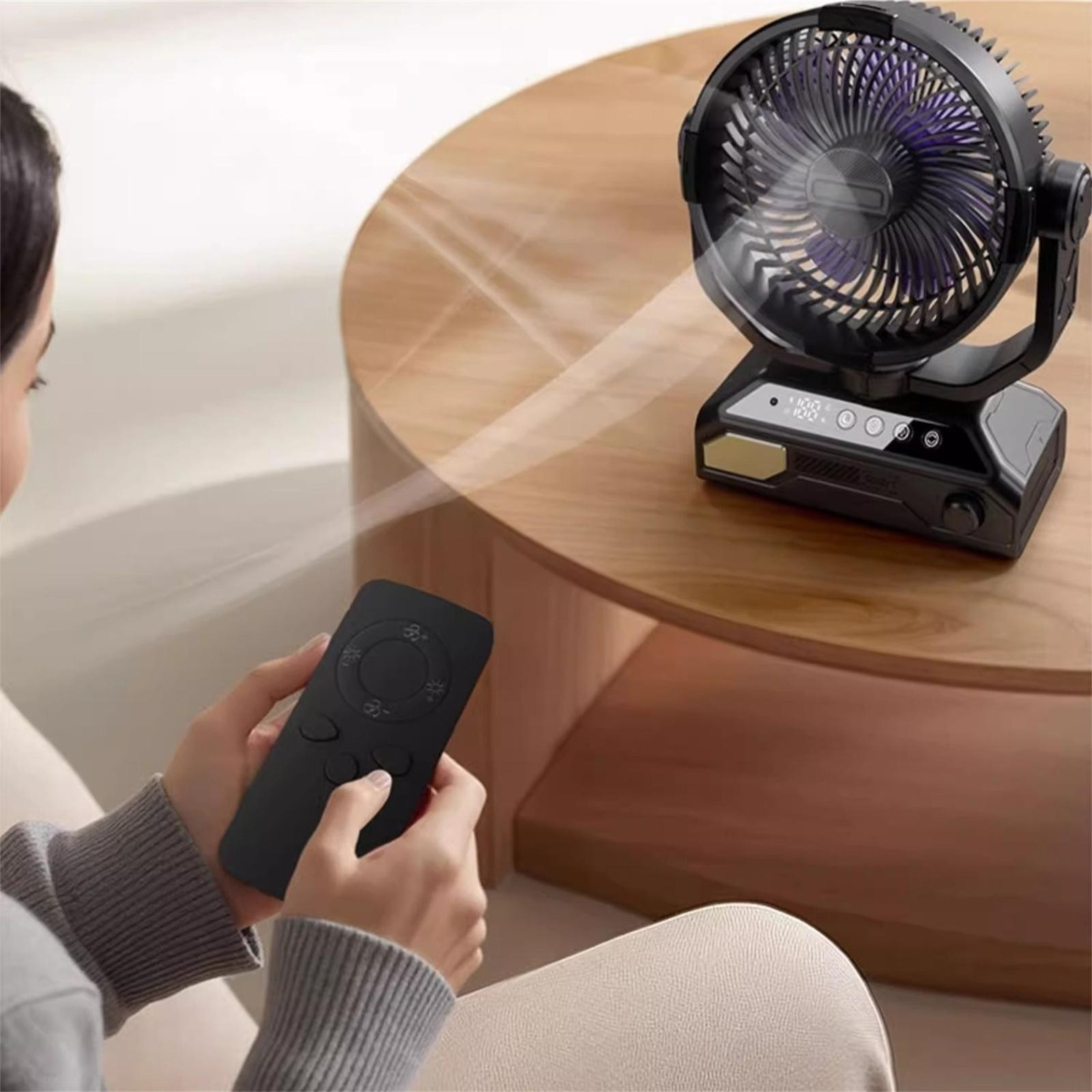 Eine Frau hält eine Fernbedienung und steuert einen schwarzen Ventilator auf einem Holztisch.