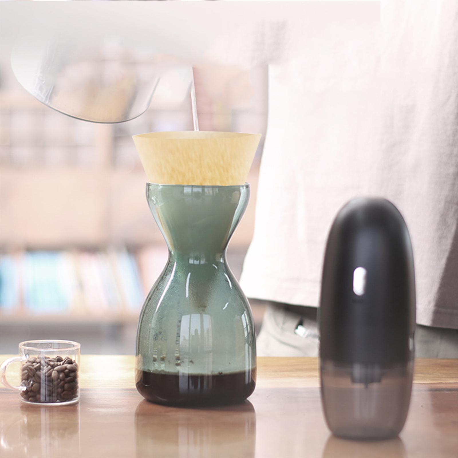 Eine Person gießt Wasser in eine Kaffeemaschine. Im Hintergrund befinden sich ein Mahlwerk und Kaffeebohnen.
