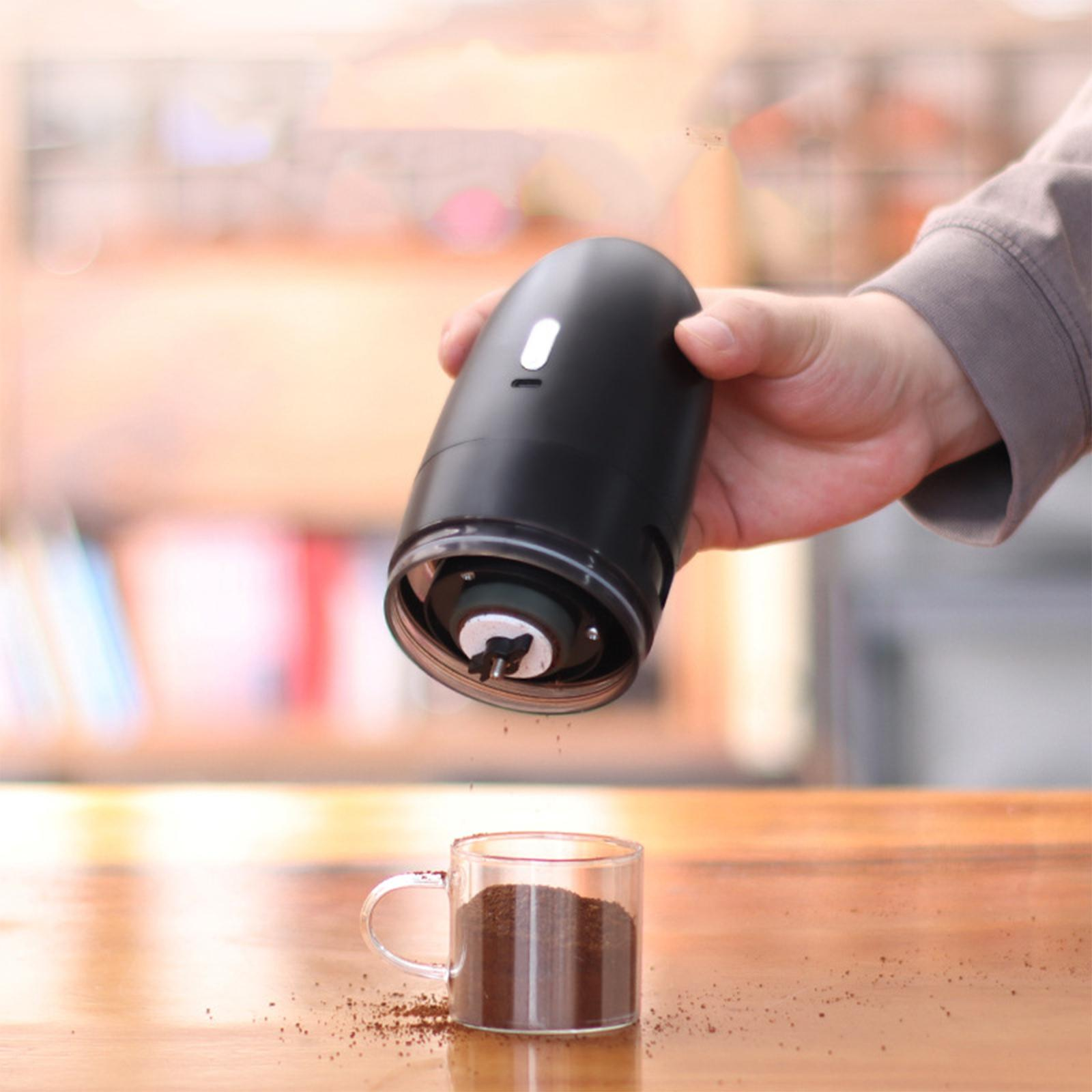 Eine Hand, die einen schwarzen elektrischen Mahlwerk über einer Glastasse mit Kaffeesatz hält.